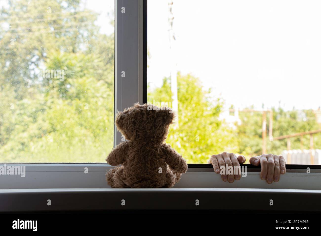 Le mani dei bambini si tengono sulla finestra dal lato della strada, e un orsacchiotto siede sulla finestra, suicidio, le mani fuori dalla finestra, suicidio Foto Stock