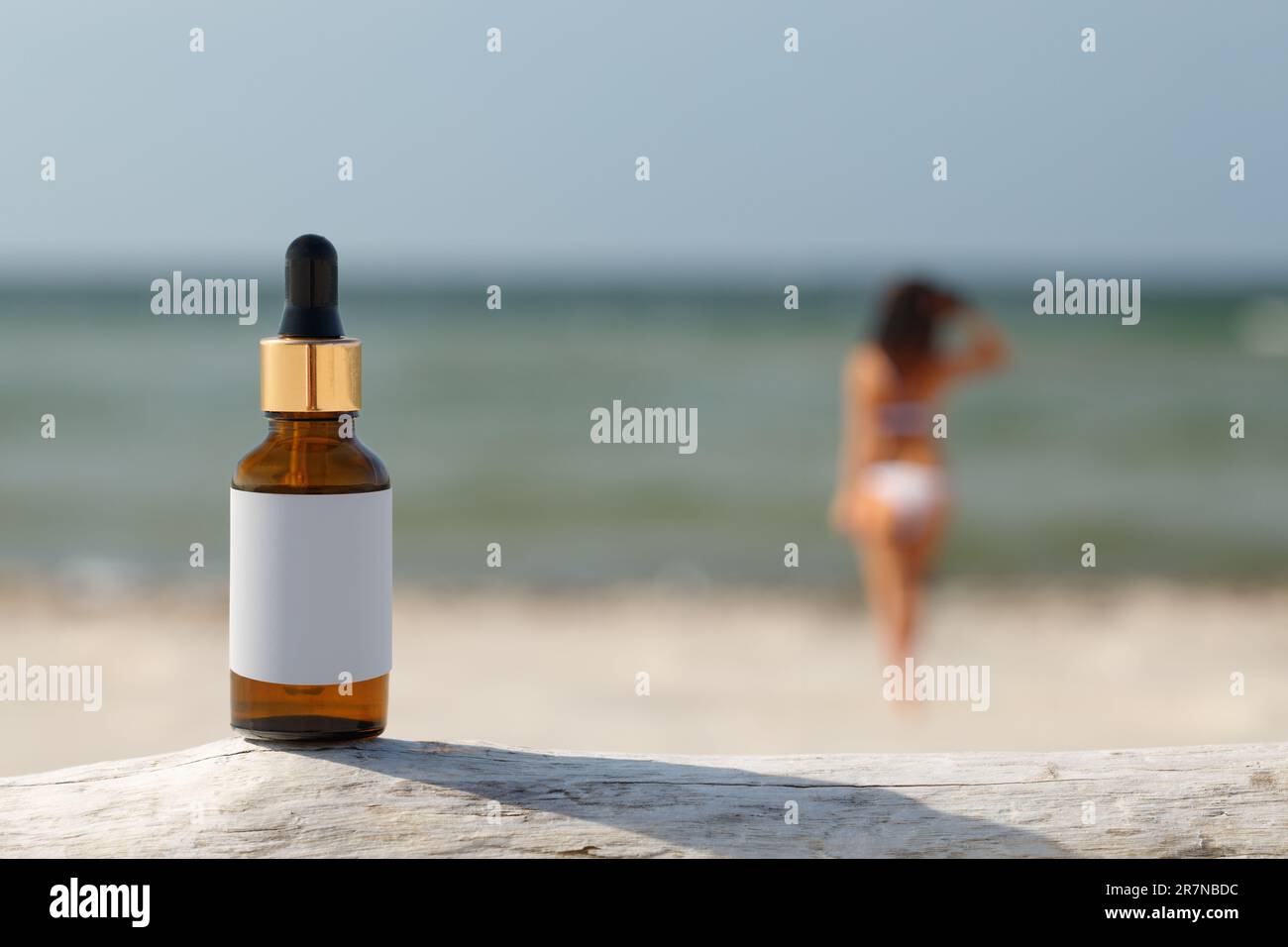 Concetto naturale di difesa del sole. Bottiglia contagocce sulla spiaggia. La silhouette sfocata di una donna, il concetto di protezione della pelle. Foto Stock