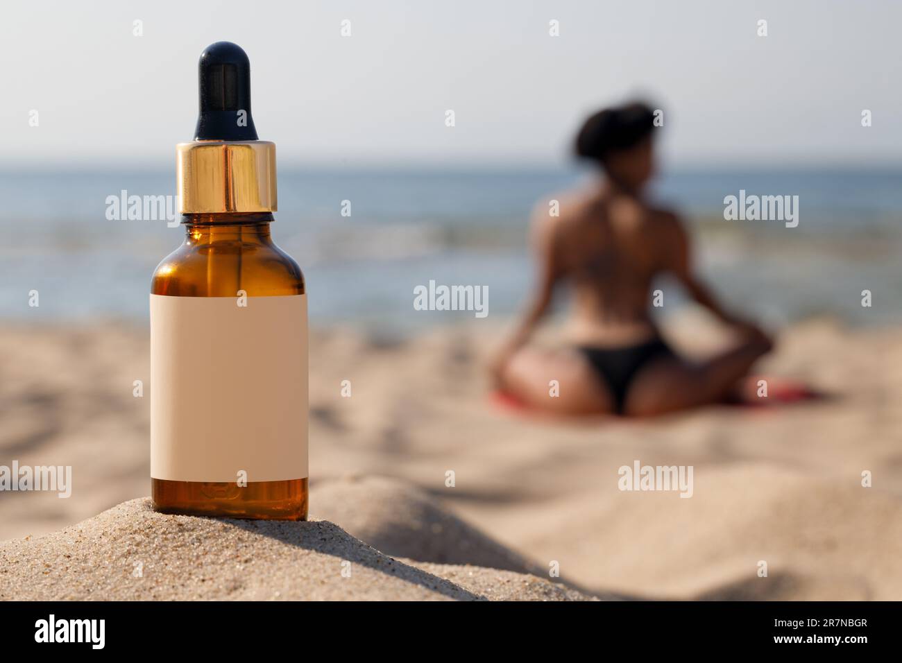 Bottiglia contagocce in spiaggia. Concetto naturale di protezione solare. La silhouette sfocata di una donna, il concetto di protezione della pelle. Foto Stock