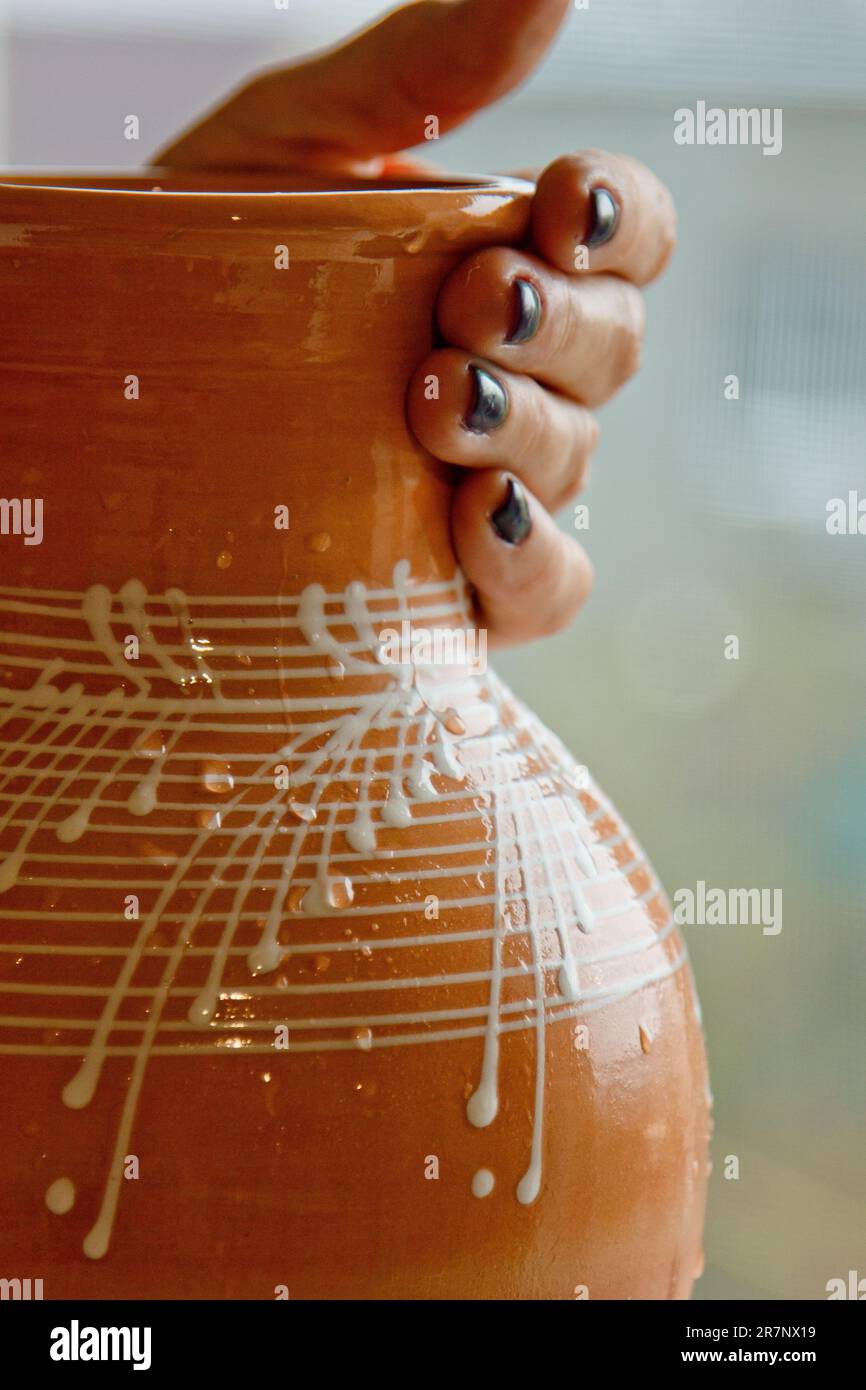 caraffa in terracotta smaltata bianca in mani femminili. primi piatti in ceramica su sfondo sfocato. verticale. Foto Stock