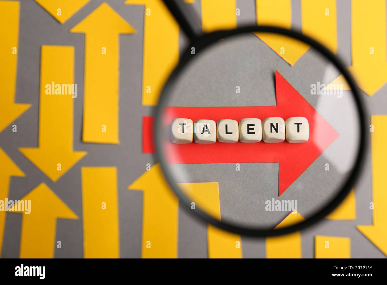 Processo di reclutamento, ricerca dipendente. Vista attraverso la lente d'ingrandimento di freccia di carta rossa e la parola Talent fatta di cubi di legno tra quelli gialli o Foto Stock