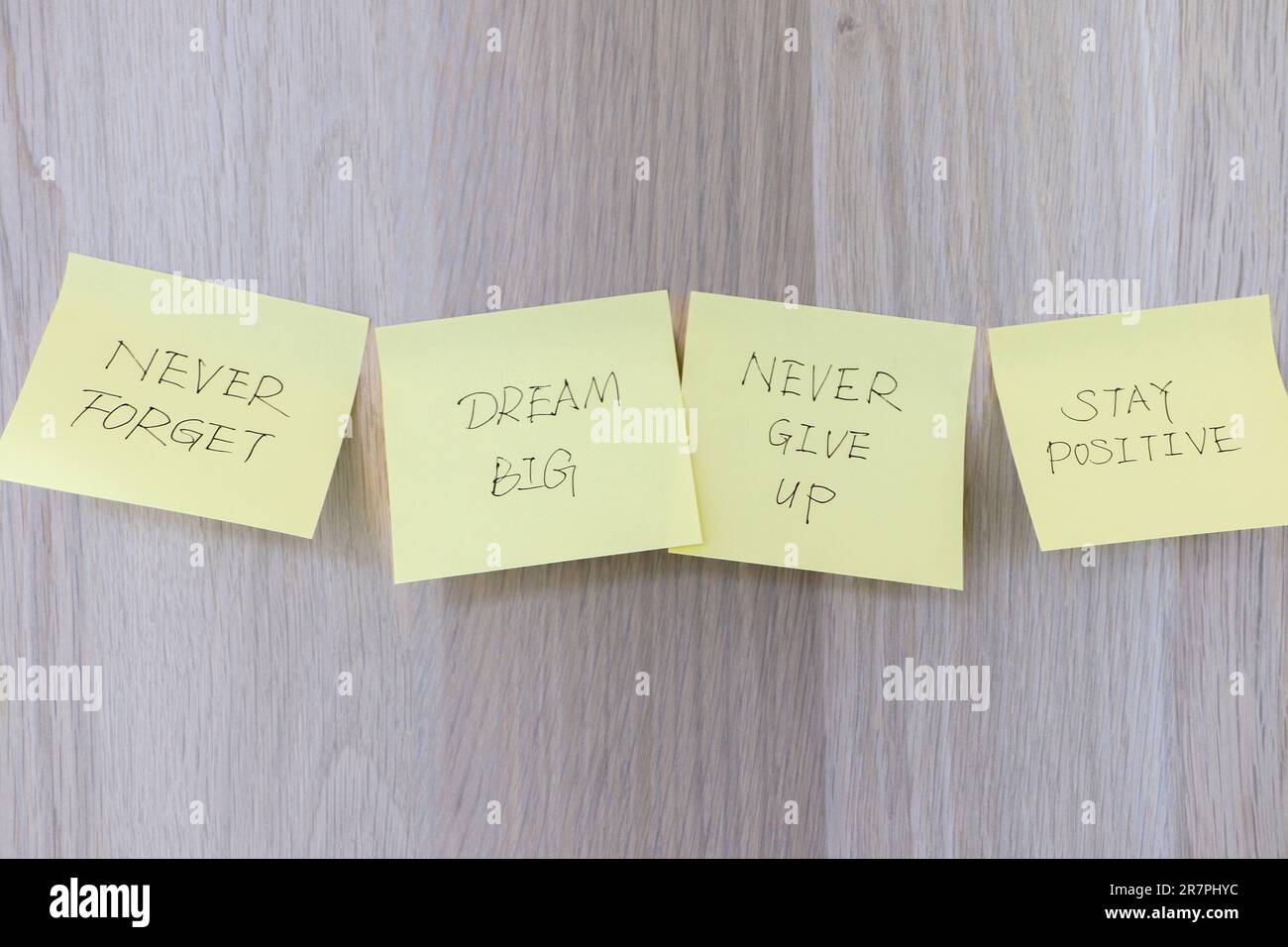 Concetto di ispirazione, quattro appunti adesivi gialli attaccati sulla scrivania di legno con messaggi motivazionali che ricordano di sognare in grande, non arrendersi mai e rimanere in posa Foto Stock