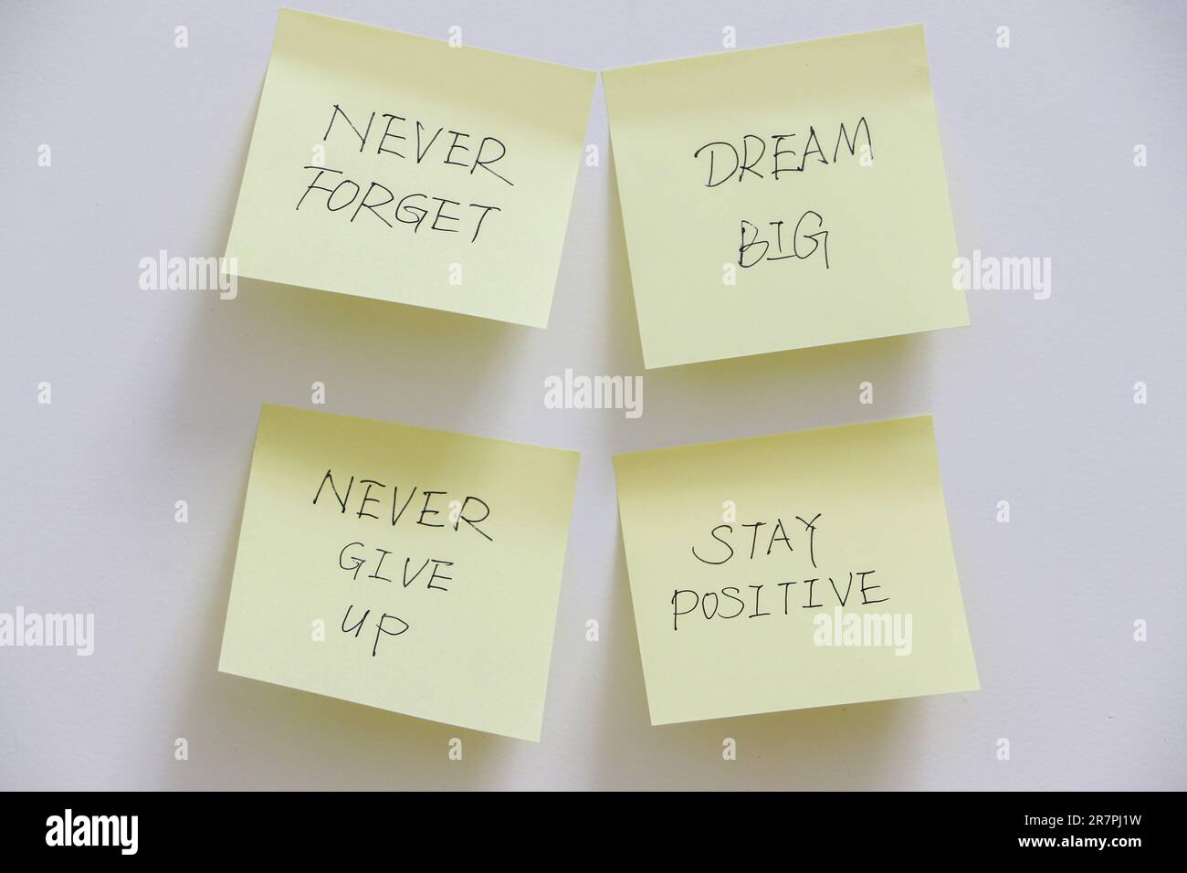 Concetto di motivazione, quattro note adesive gialle sulla parete bianca con messaggi ispiratori per ricordarti di sognare in grande, non arrenderti mai e rimanere positivo Foto Stock