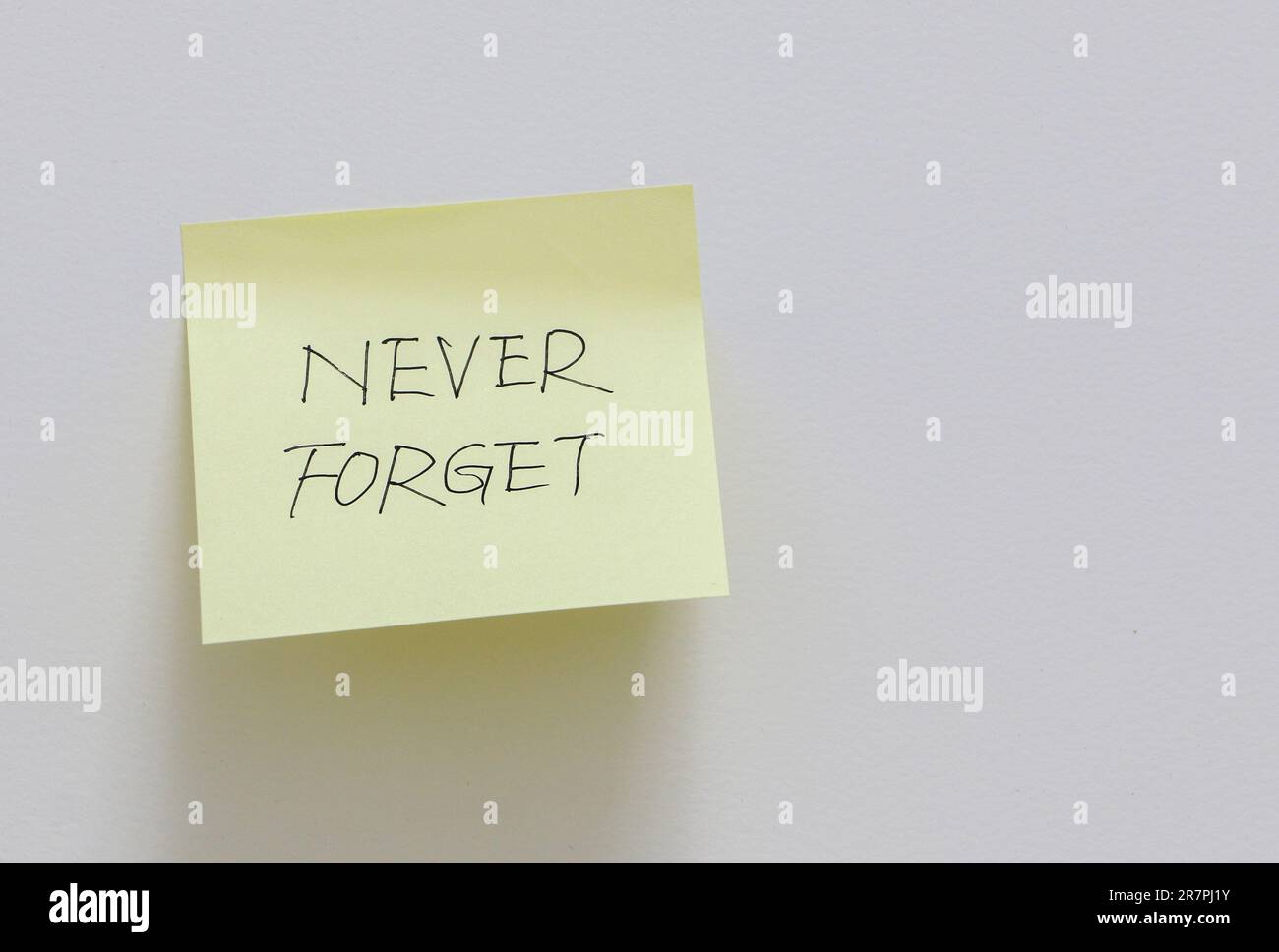Nota adesiva gialla attaccata su una parete bianca con un promemoria per non dimenticare mai, concetto di memoria Foto Stock