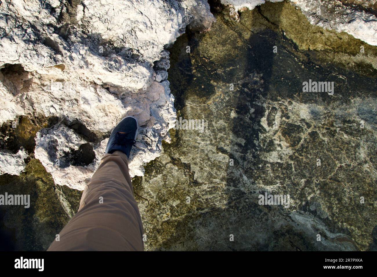 MELLIEHA, MALTA - 01 GENNAIO 2020: Un piede dell'uomo attraversa una piccola piscina rocciosa con acqua salata su una costa rocciosa di Malta vicino alla Laguna dei Coralli Foto Stock
