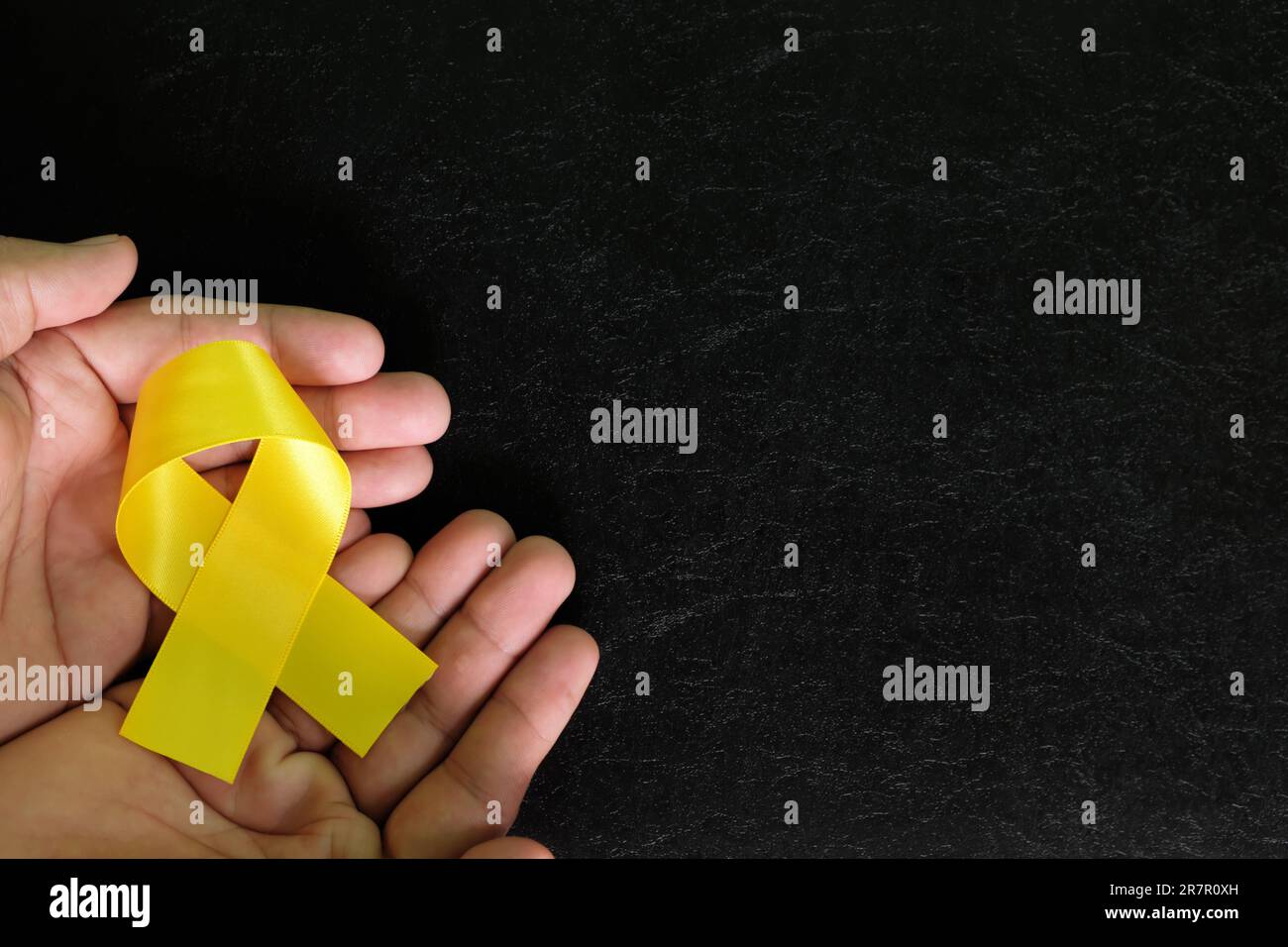 Mani umane con nastro giallo su sfondo nero scuro. Consapevolezza del cancro osseo e prevenzione del suicidio concetto di speranza. Foto Stock