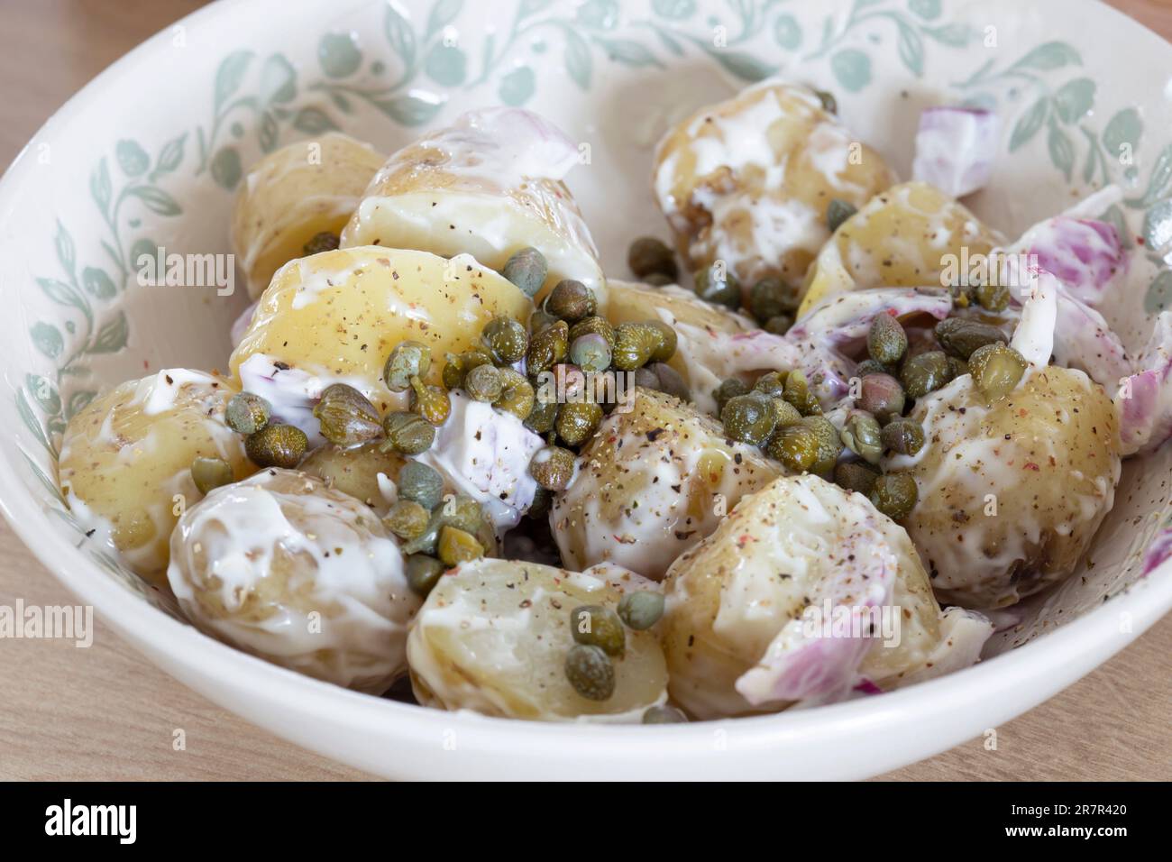 Insalata di patate fatta in casa con cipolla rossa e capperi in una ciotola. Su un piano di lavoro in legno Foto Stock