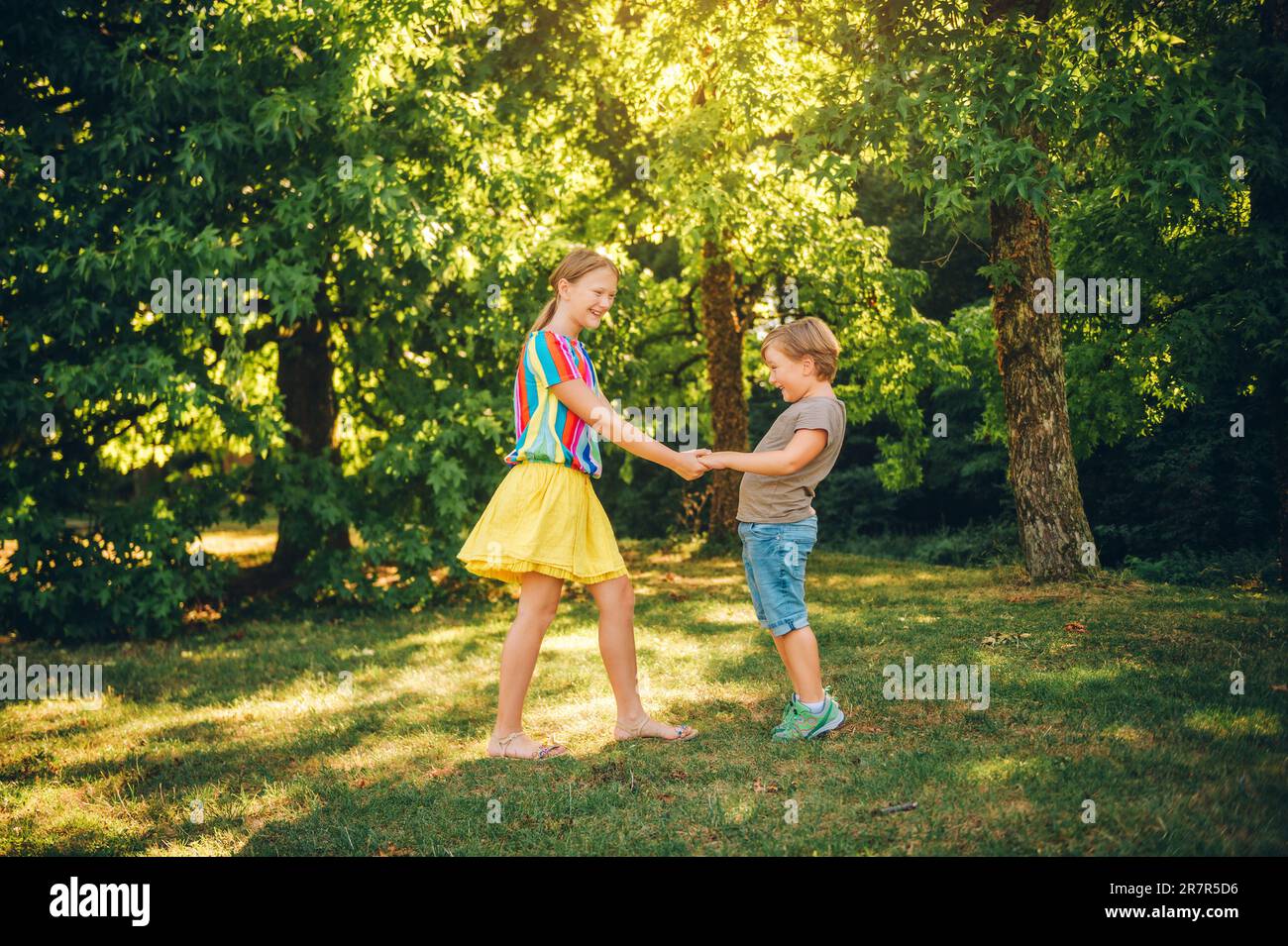 Gruppo di due bambini che giocano insieme nel parco estivo, tenendo le mani, girando insieme Foto Stock