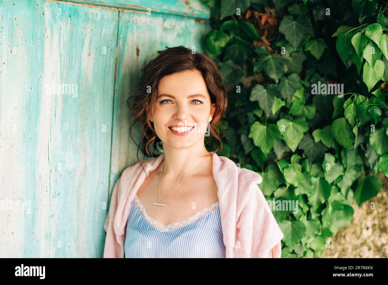 Ritratto all'aperto di bella giovane donna con capelli scuri, posa su sfondo verde Foto Stock