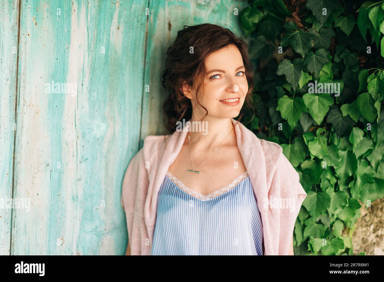 Ritratto all'aperto di bella giovane donna con capelli scuri, posa su sfondo verde Foto Stock