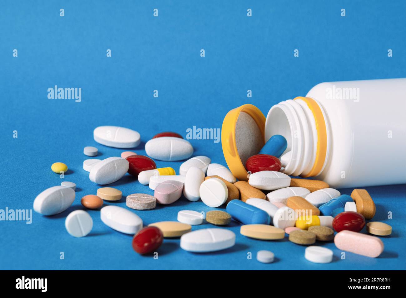 Molte pillole versate da una bottiglia di plastica. Pillole multicolore che fuoriescono da una bottiglia di plastica su sfondo blu. Una varietà di pillole e farmaci. Foto Stock