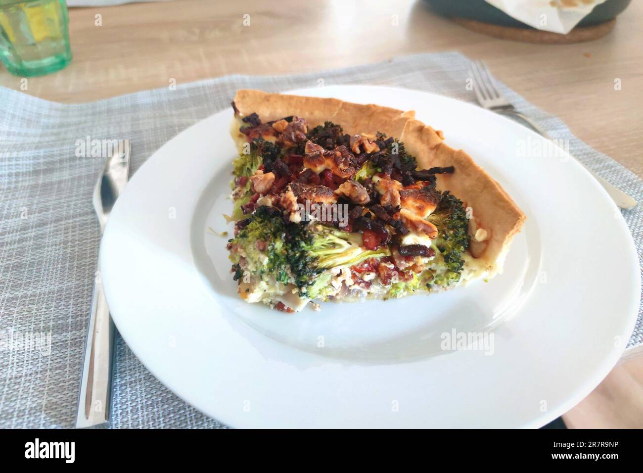Grande fetta di quiche, composta da crosta di pasta sfoglia ripiena di broccoli, pomodori e pancetta. Foto Stock