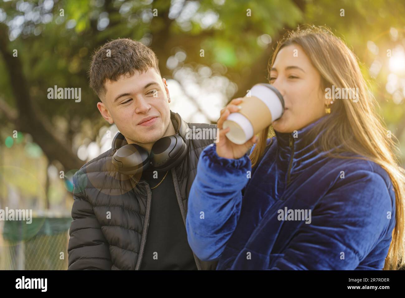Ragazzo che guarda una ragazza Latina bere caffè sulla panchina in un parco pubblico. Foto Stock