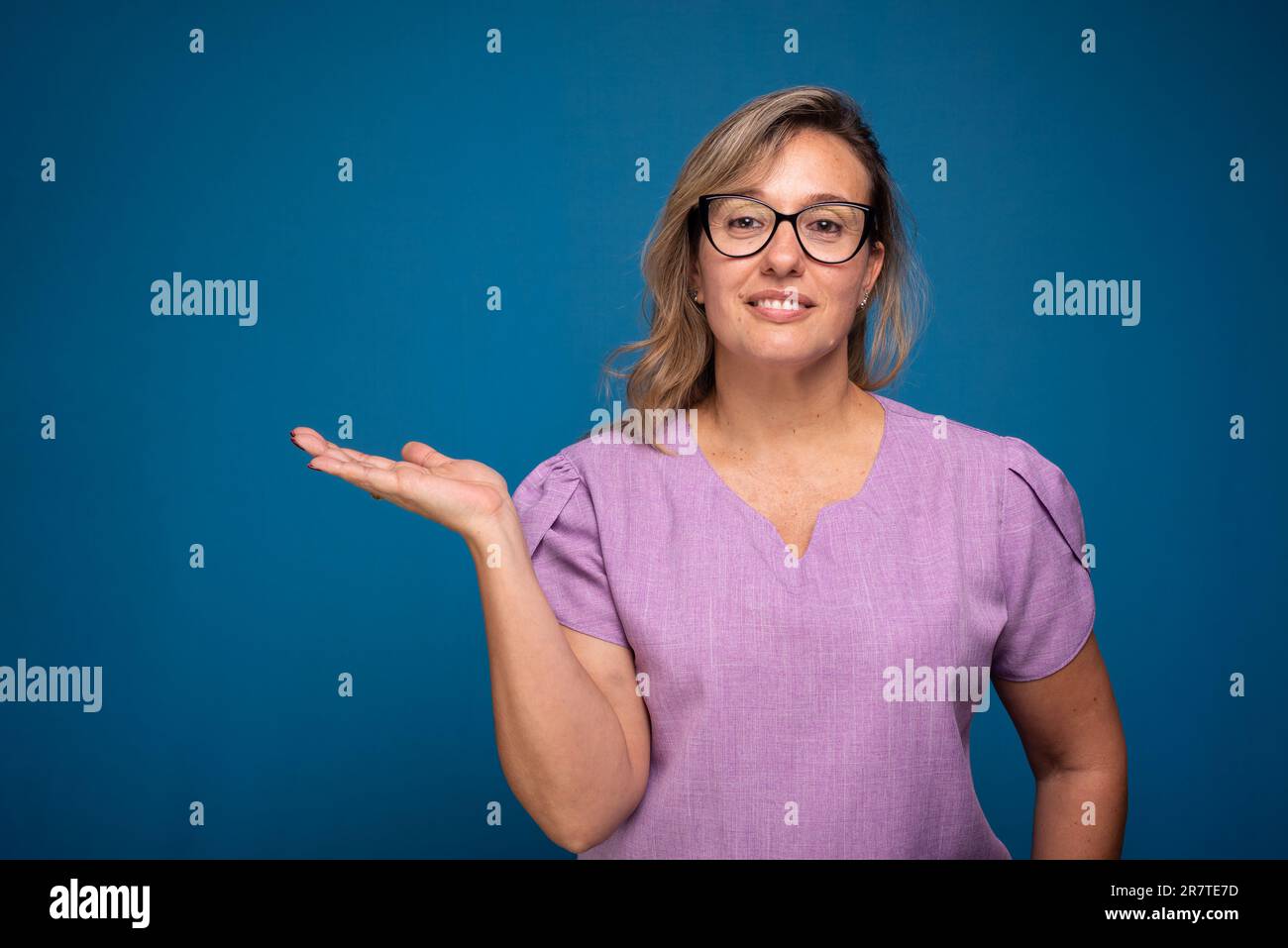Bella donna brasiliana, bionda, indossando uniforme infermiera lilla e facendo gesti di mano. Persona positiva. Isoald su sfondo blu. Foto Stock