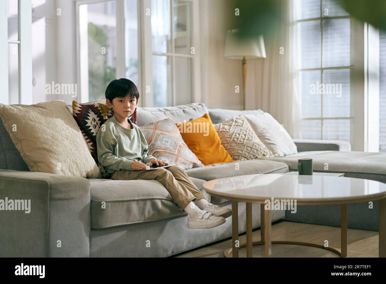 piccolo ragazzo asiatico seduto sul divano della famiglia nel soggiorno di casa, che guarda triste Foto Stock