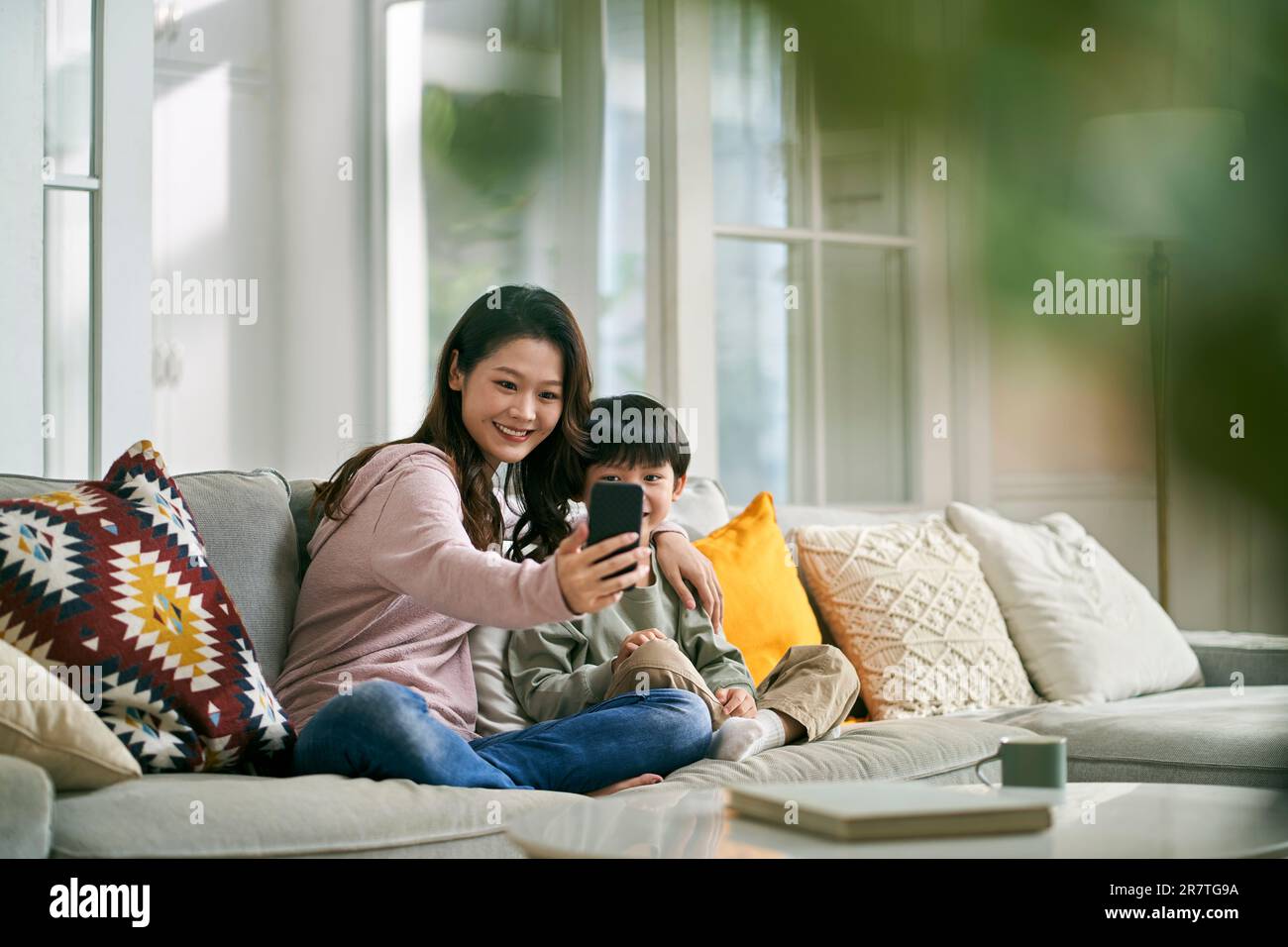 felice madre asiatica e figlio seduto sul divano di famiglia a casa con un selfie utilizzando il telefono cellulare Foto Stock
