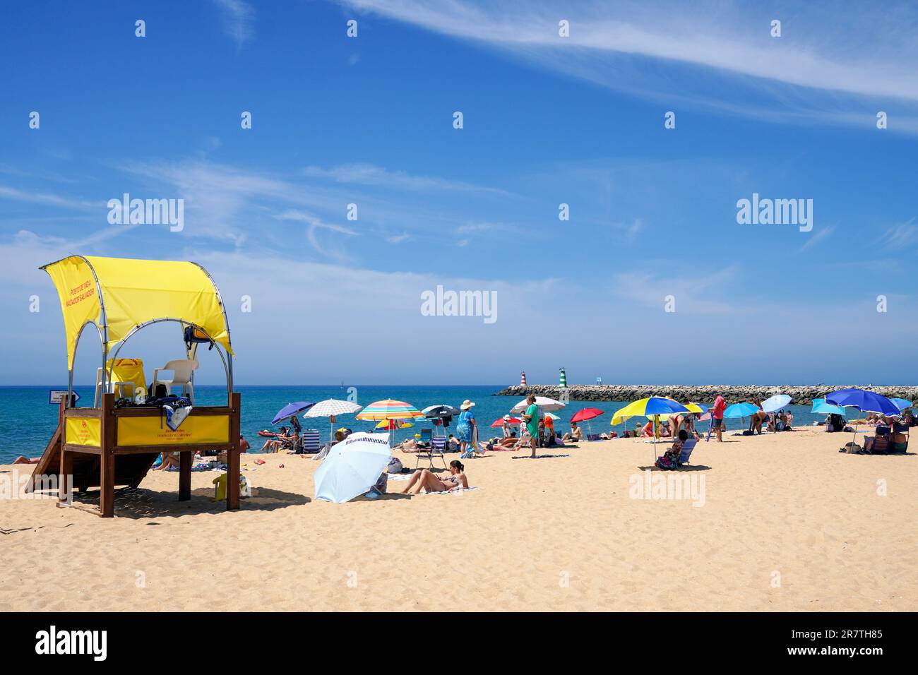 Spiaggia a Vilamoura, con turisti e bagnino stazione, e il faro alla fine del porto turistico, Algarve, Portogallo. Foto Stock