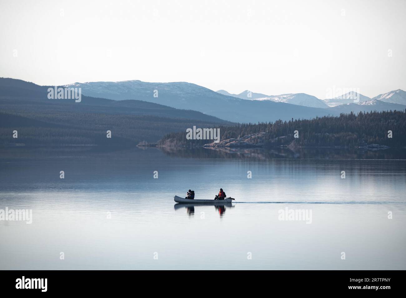 Due persone che si canoano su un lago limpido, tranquillo e mozzafiato circondato da montagne e natura selvaggia nel Canada settentrionale. Foto Stock