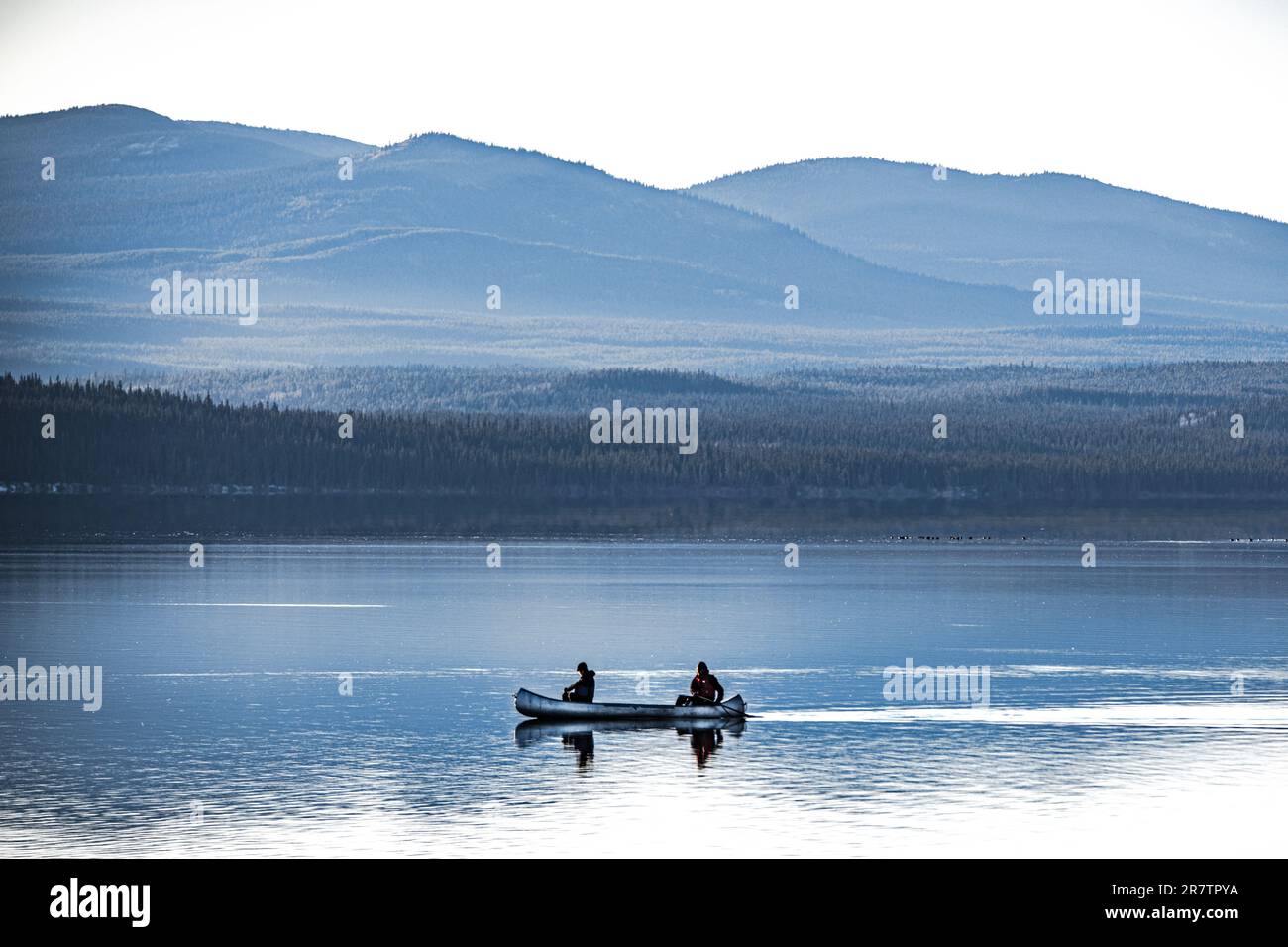 Due persone che si canoano su un lago limpido, tranquillo e mozzafiato circondato da montagne e natura selvaggia nel Canada settentrionale. Foto Stock