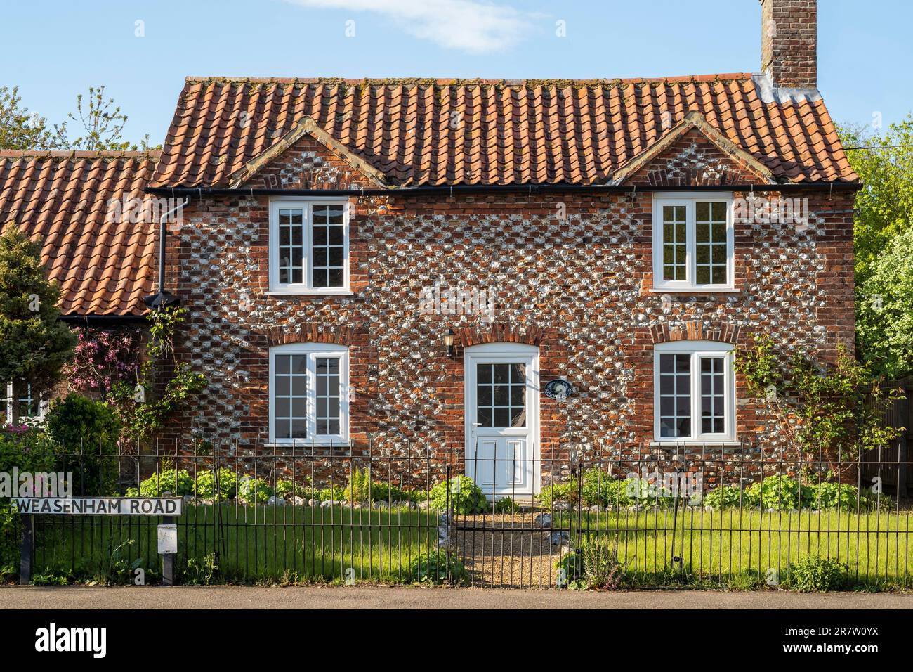 Tradizionale grazioso cottage in mattoni e selce con tetto piastrellato e ringhiere in metallo e cartello stradale nel pittoresco villaggio di Great Massingham a Norfolk, Inghilterra Foto Stock