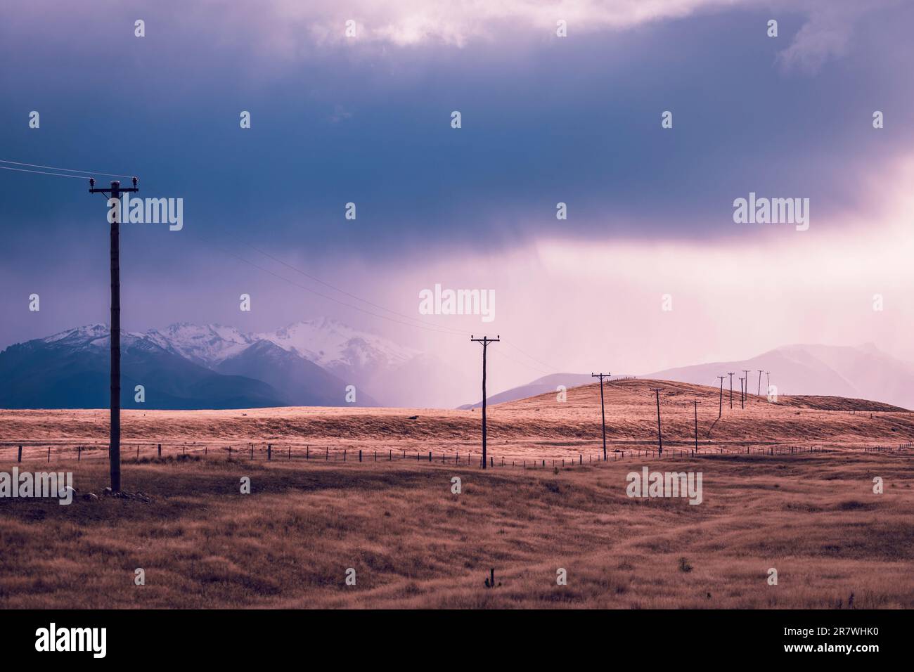 Fotografia di pali telefonici che attraversano una valle contro montagne innevate sull'Isola Sud della Nuova Zelanda Foto Stock