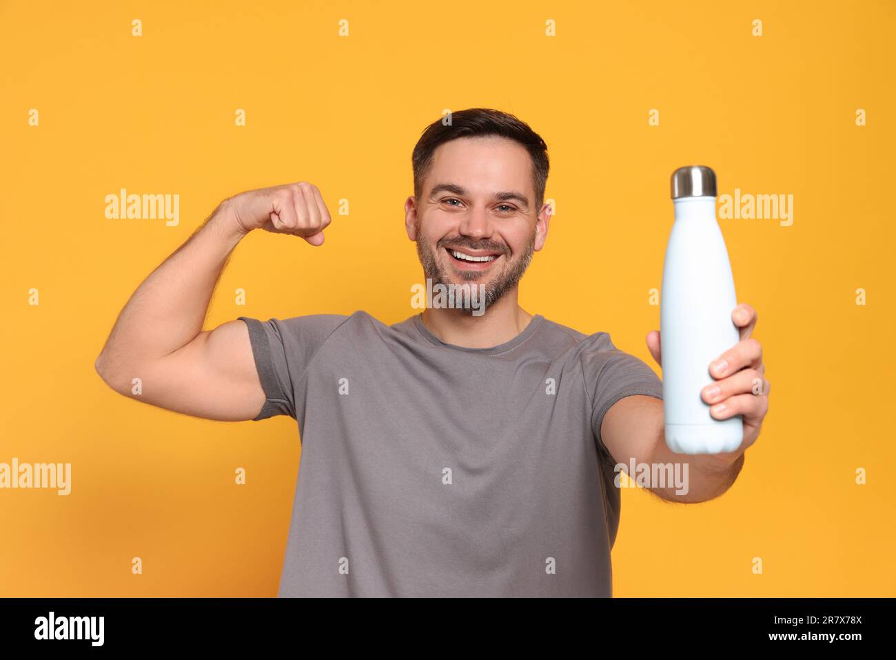 Uomo felice che tiene la bottiglia di termo e che mostra il braccio su sfondo arancione Foto Stock