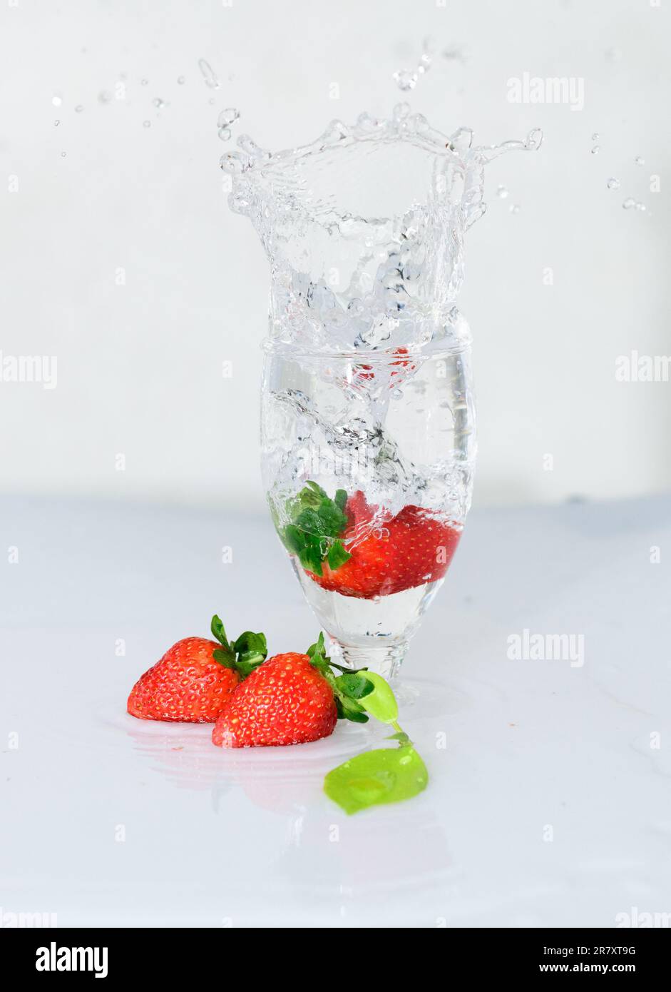 La fragola cade su un bicchiere di vino, si congela il movimento dell'acqua, fondo bianco. Foto Stock