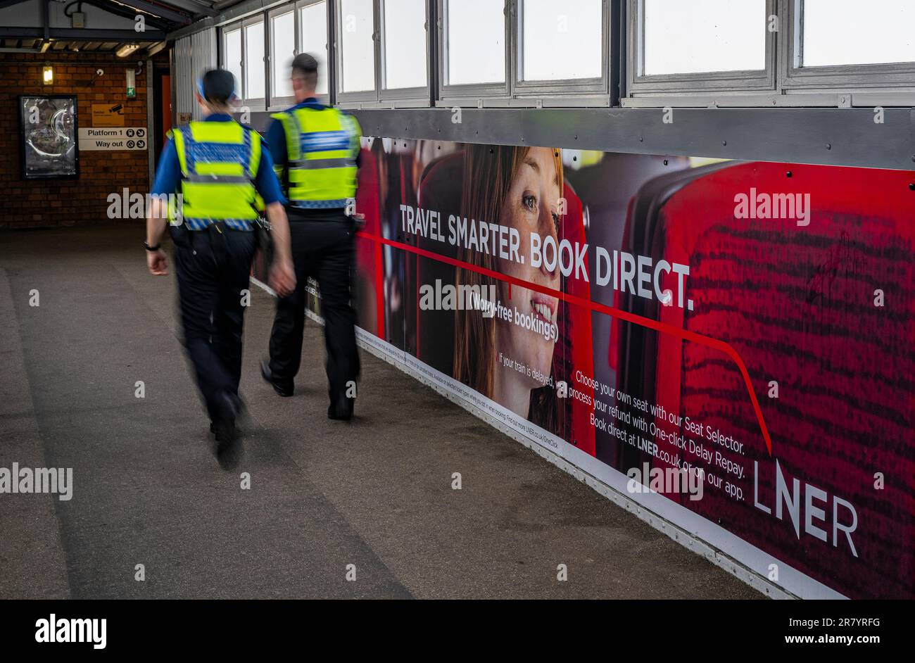 I poliziotti della polizia dei trasporti britannici che camminano davanti ad un'accaparramento pubblicitario per la ferrovia nord-orientale di Londra (LNER) per viaggiare più astuti e prenotare direttamente Foto Stock