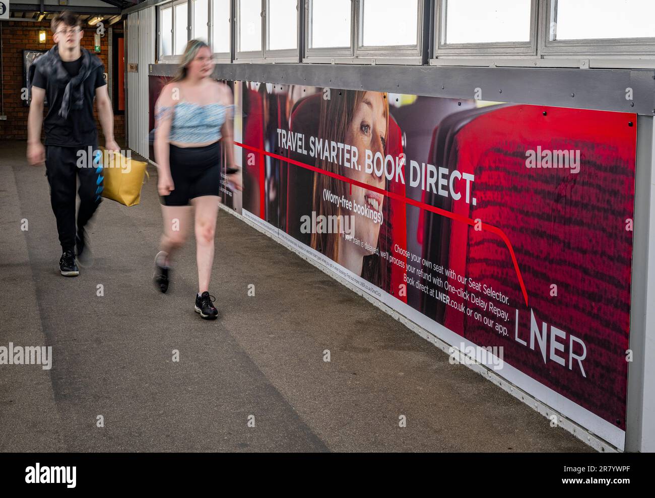 Una giovane coppia che passa davanti a una pubblicità accaparrarsi per London North Eastern Railway (LNER) per viaggi più intelligenti e prenotare direttamente Foto Stock