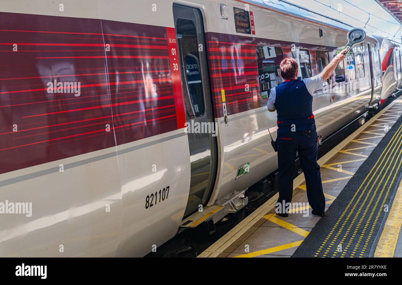 Grantham Train Station – Una direttrice o guardia femminile che spedisce un treno Azuma London North Eastern (LNER) dalla piattaforma Foto Stock
