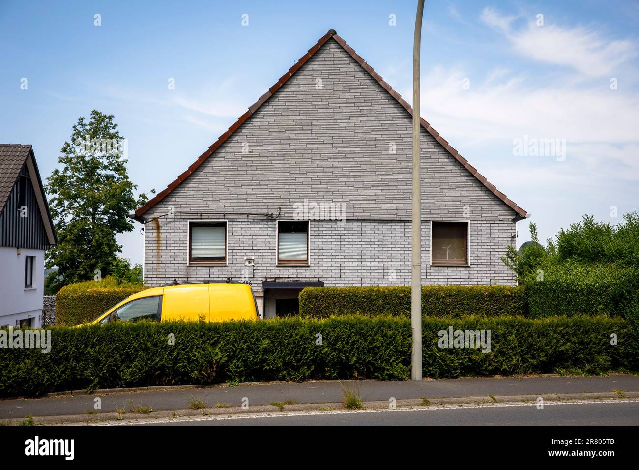 Un'auto gialla si trova dietro una siepe di fronte a una casa in mattoni grigi a Gevelsberg-Silschede, Renania settentrionale-Vestfalia, Germania. ein gelbes Auto steht suggerimento Foto Stock