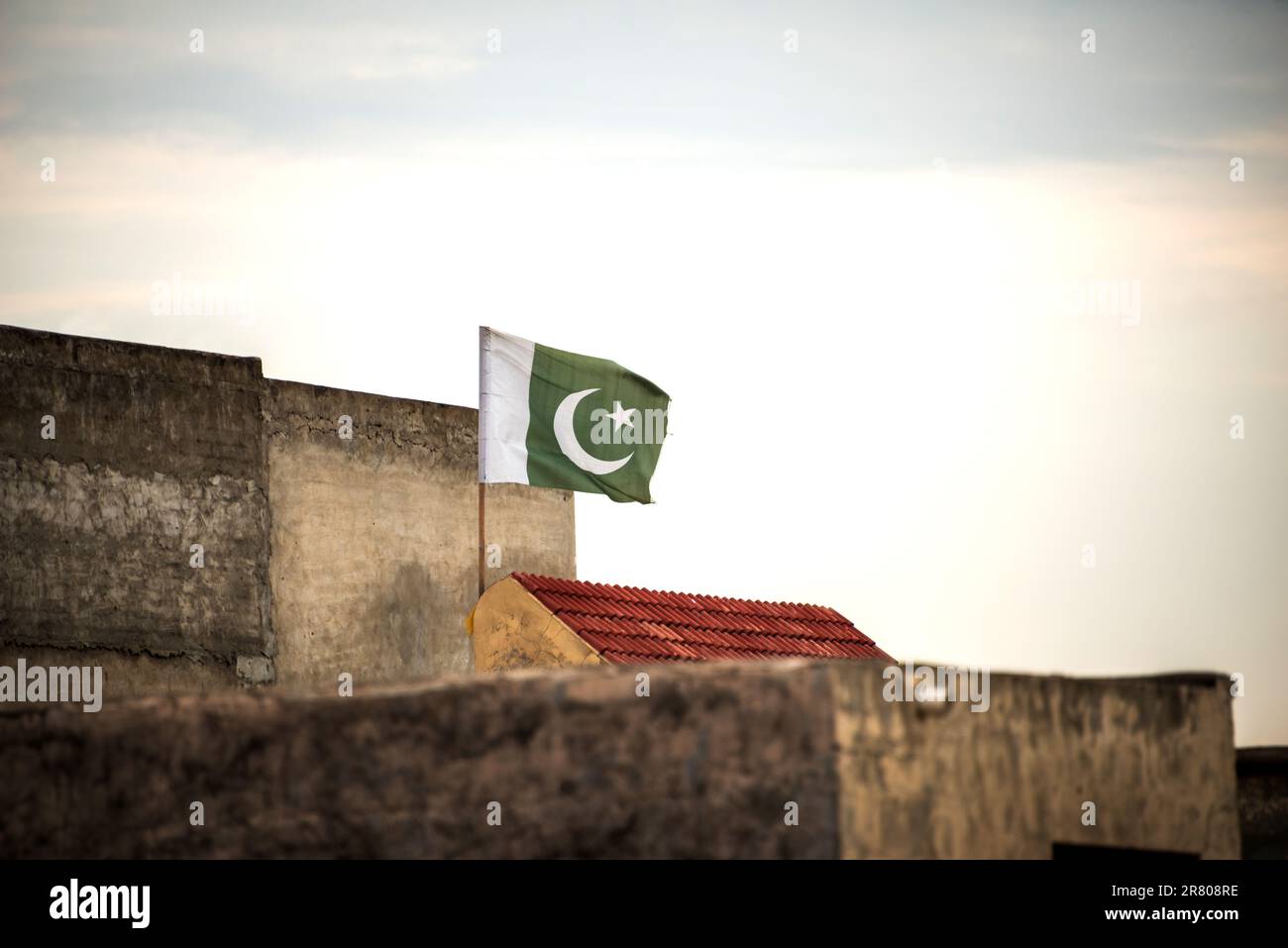 Una bandiera pakistana sta sventolando sul tetto di una casa in un cielo nuvoloso. Foto Stock