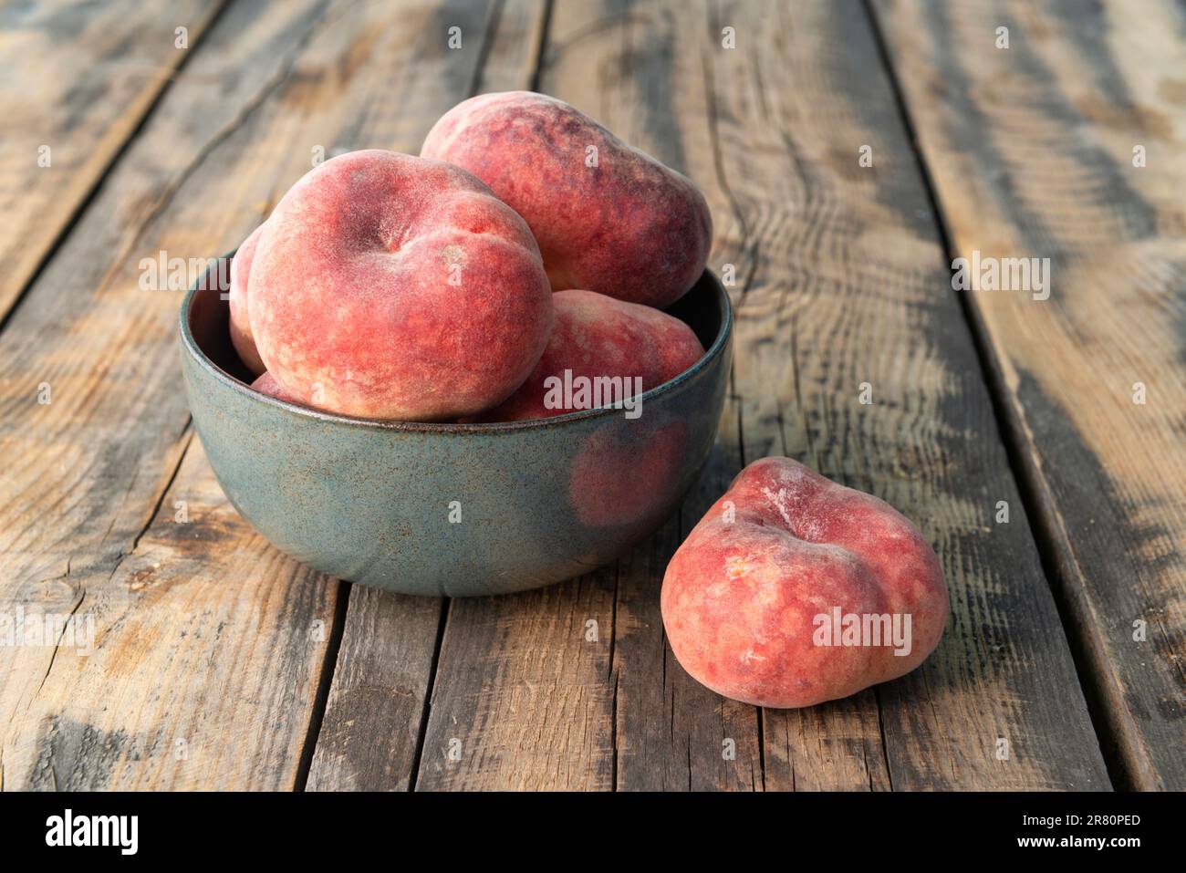 Ciotola in ceramica con pesche di ciambella su un tavolo di legno Foto Stock