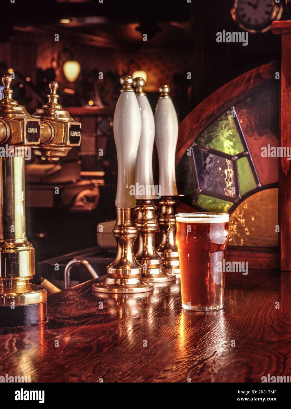 La pinta di bitter servita al bar in legno superficie di una calda e tipica e tradizionale inglese invitante public house, con birra lager e maniglie della pompa dietro Foto Stock