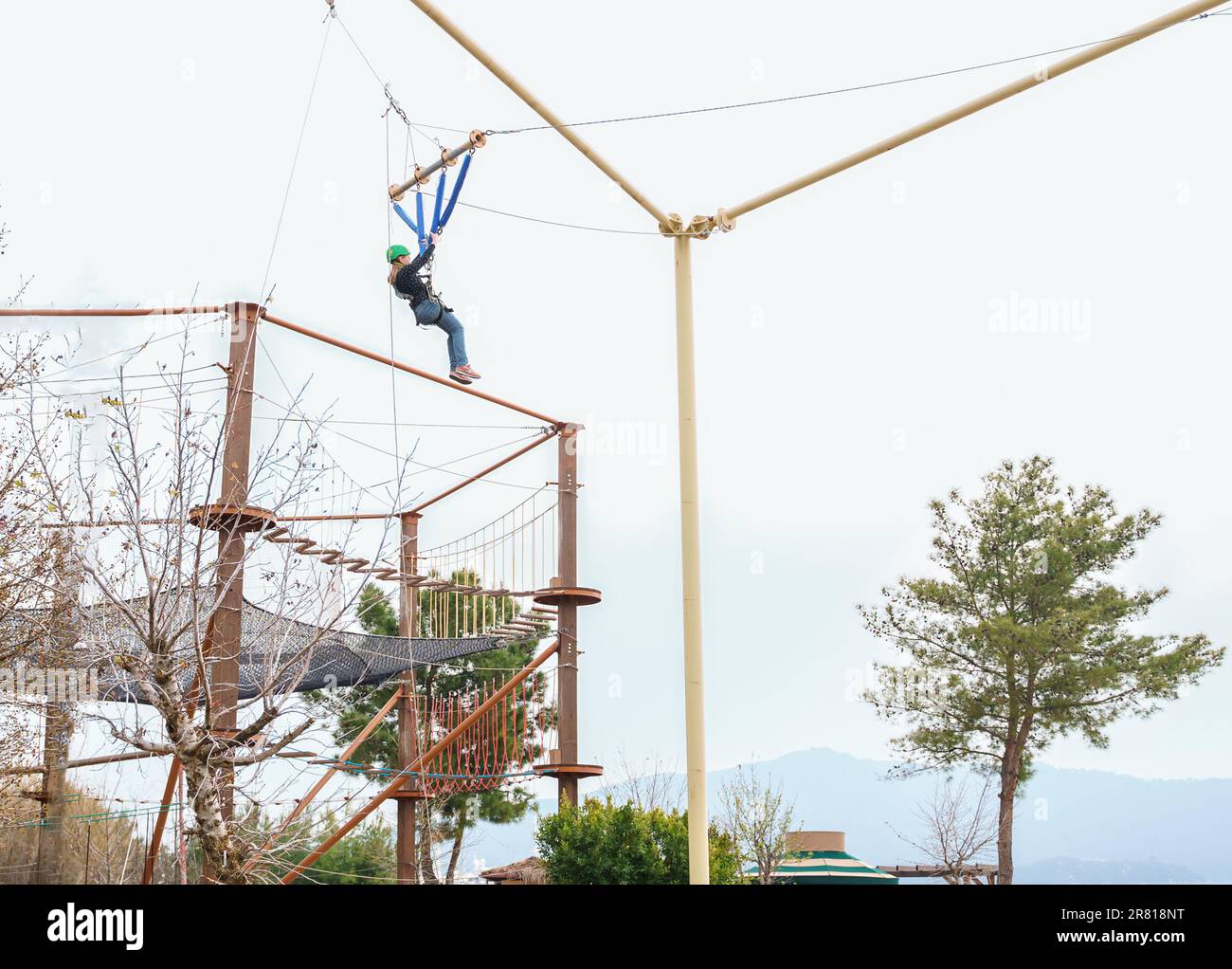 Ragazza adolescente bungee volare in corda parco divertimenti. Imbracatura da arrampicata, casco di sicurezza sportivo verde. Percorso ostacolo sospeso. Bambini Foto Stock