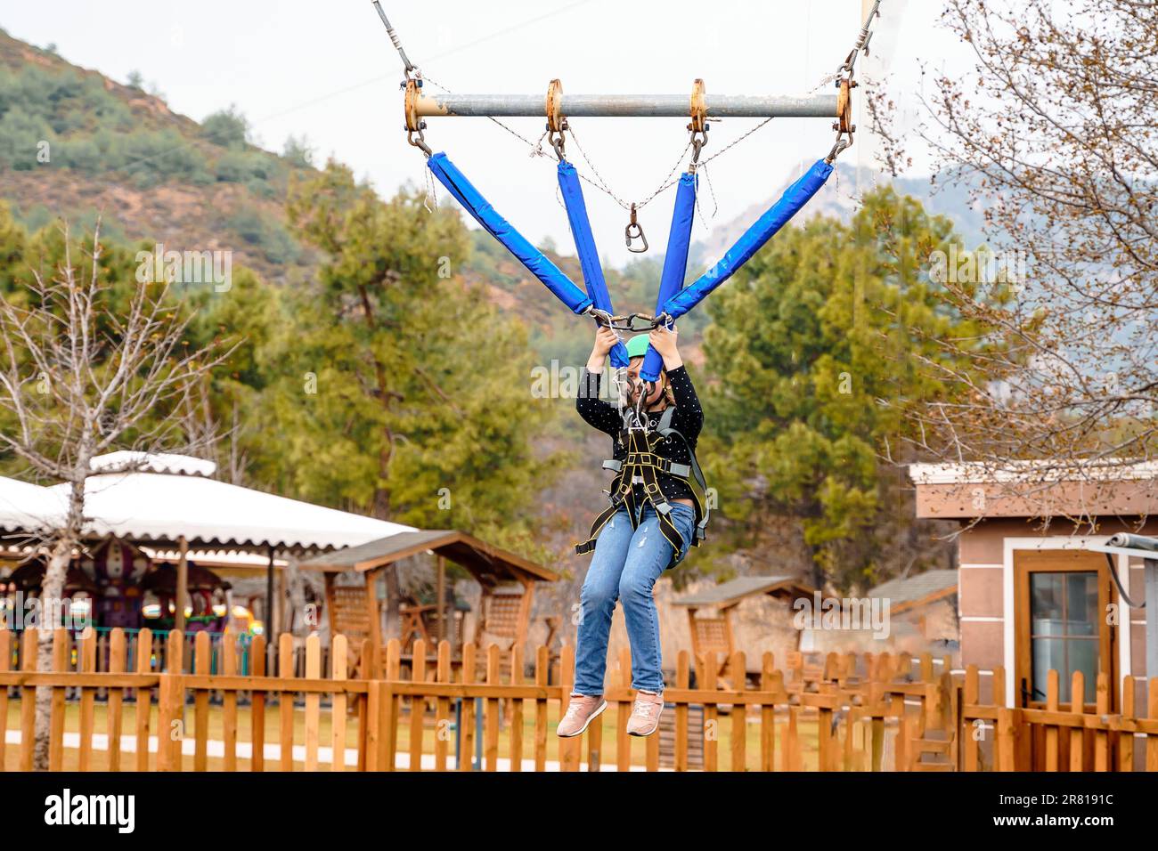 Ragazza adolescente bungee volare in corda parco divertimenti. Imbracatura da arrampicata, casco di sicurezza sportivo verde. Percorso ostacolo sospeso. Bambini Foto Stock