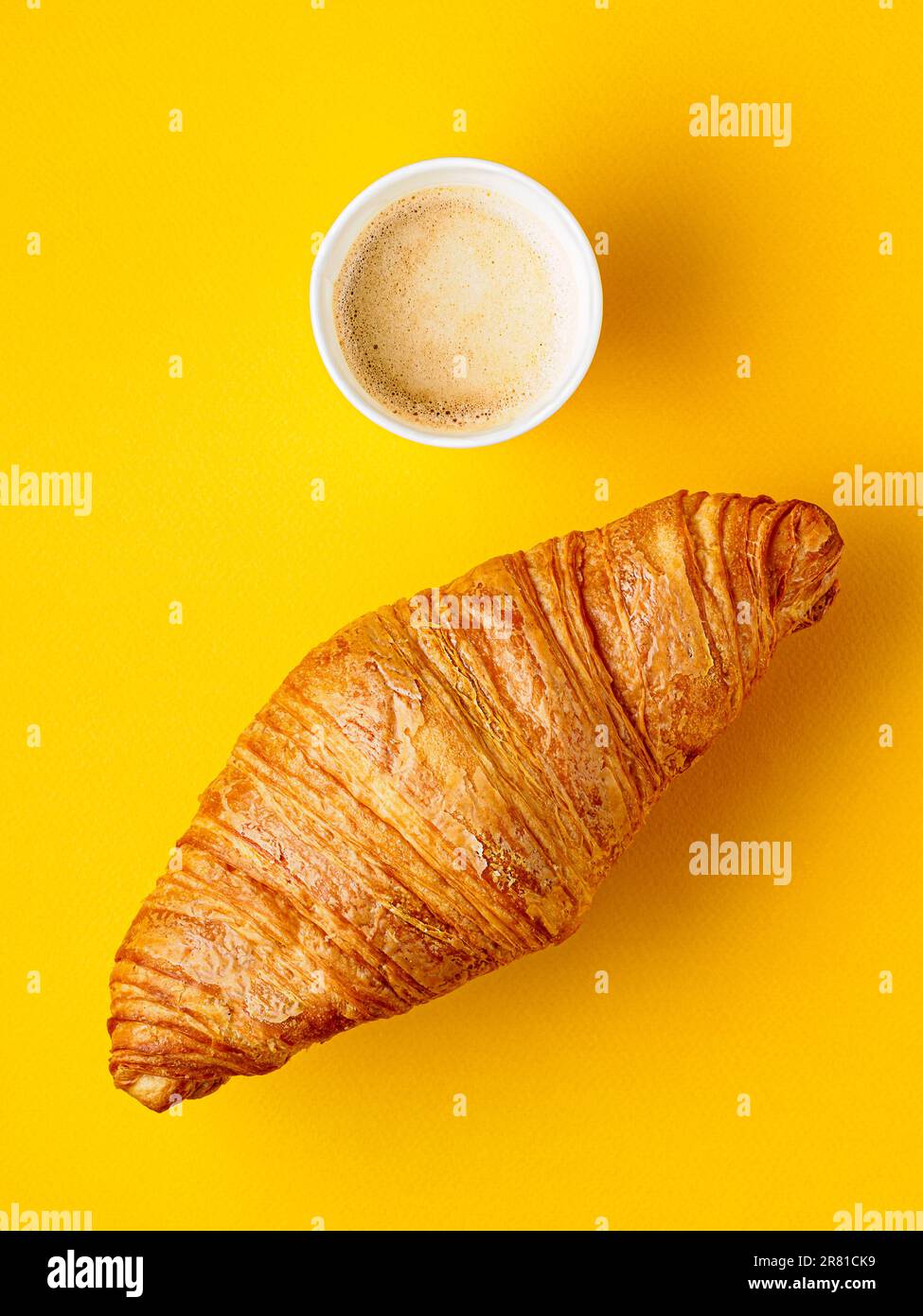 Vista dall'alto su una tazza di carta di caffè e croissant su sfondo giallo. Concetto di colazione. Foto Stock