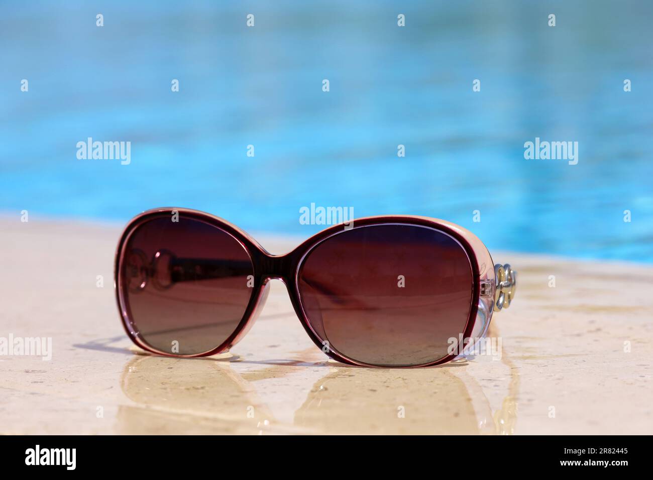 Occhiali da sole sul bordo della piscina con acqua blu. Vacanza al sole sulla spiaggia Foto Stock