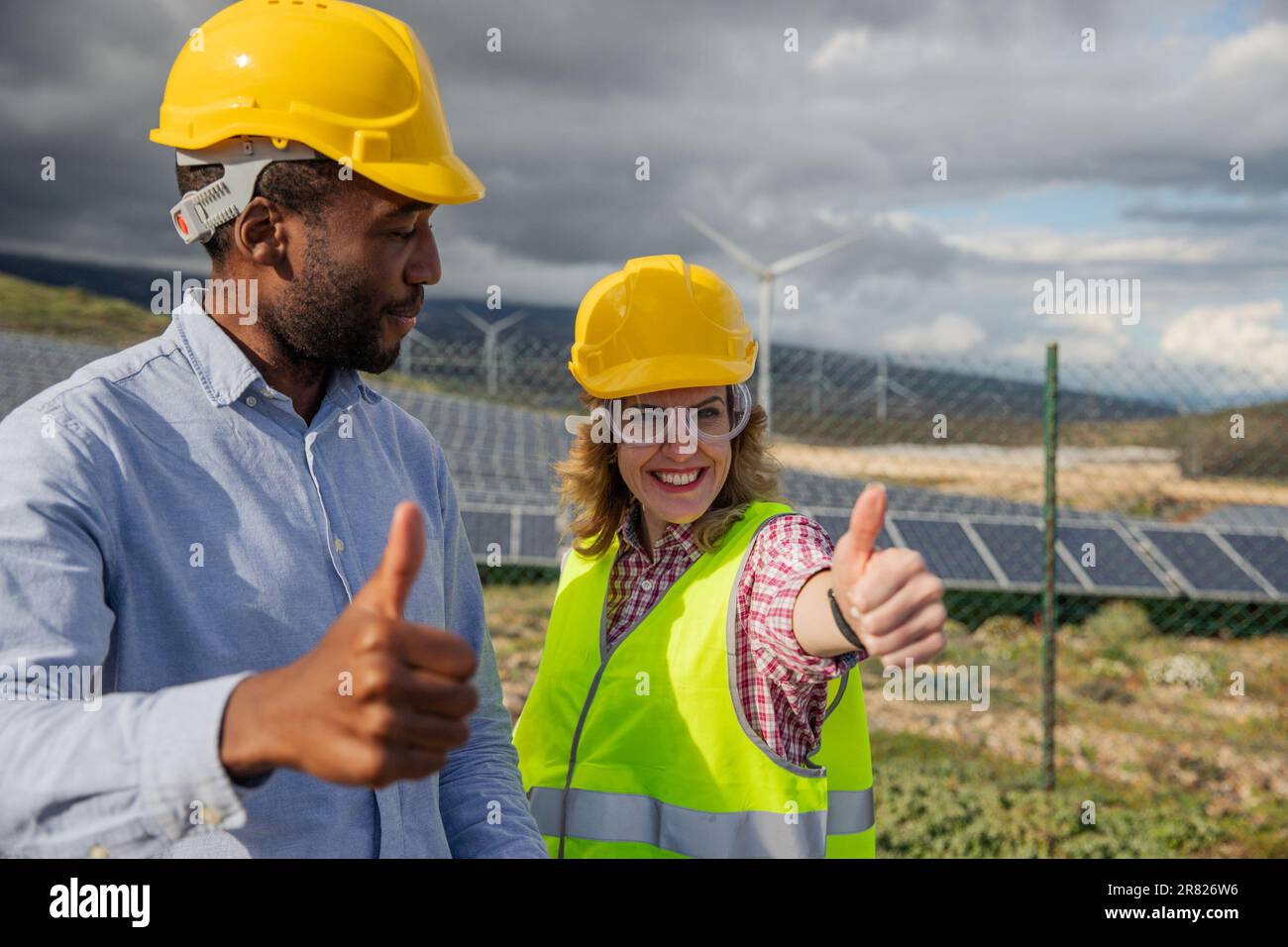 Due ingegneri soddisfatti in una centrale di energia solare al lavoro mostrano i pollici in su, gruppo multietnico Foto Stock Due ingegneri soddisfatti in una centrale di energia solare al lavoro mostrano i pollici in su, gruppo multietnico Foto Stock