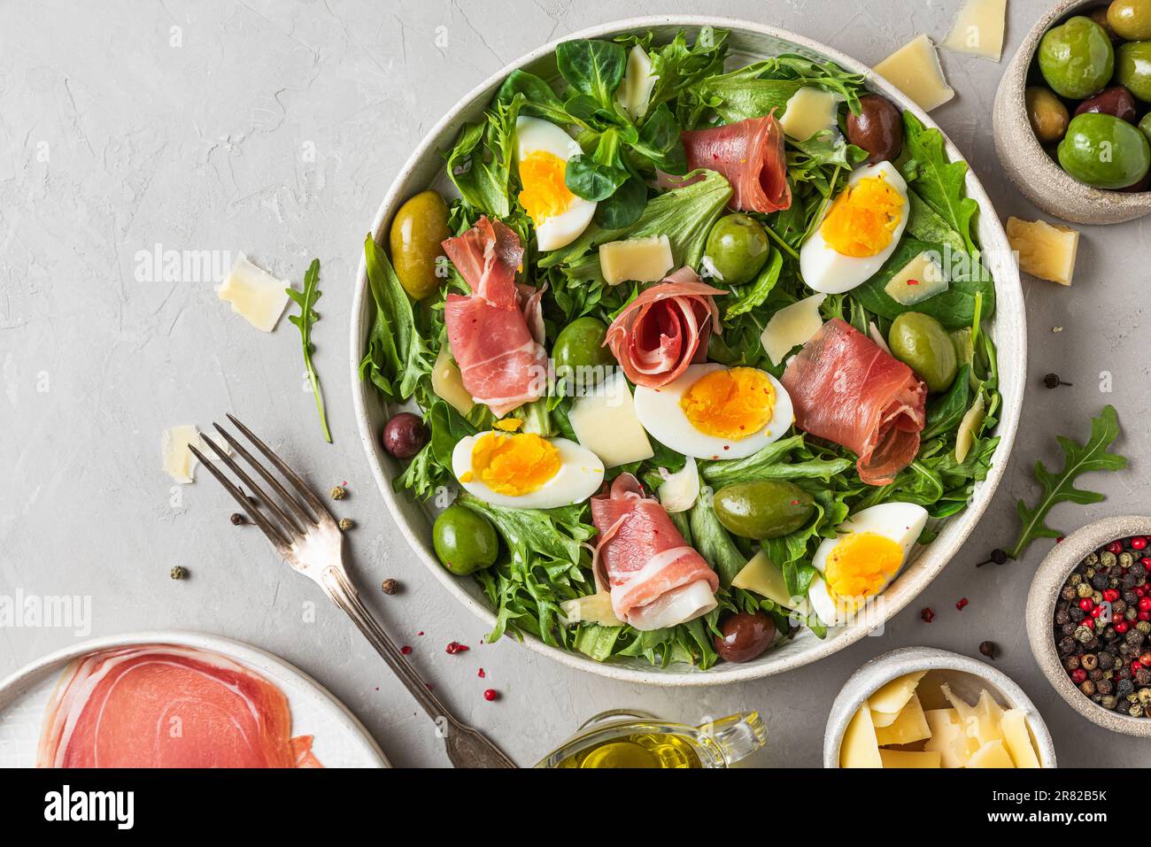 Insalata di prosciutto con parmigiano, olive, uova e rucola in un piatto su fondo grigio. Cucina italiana. vista dall'alto Foto Stock
