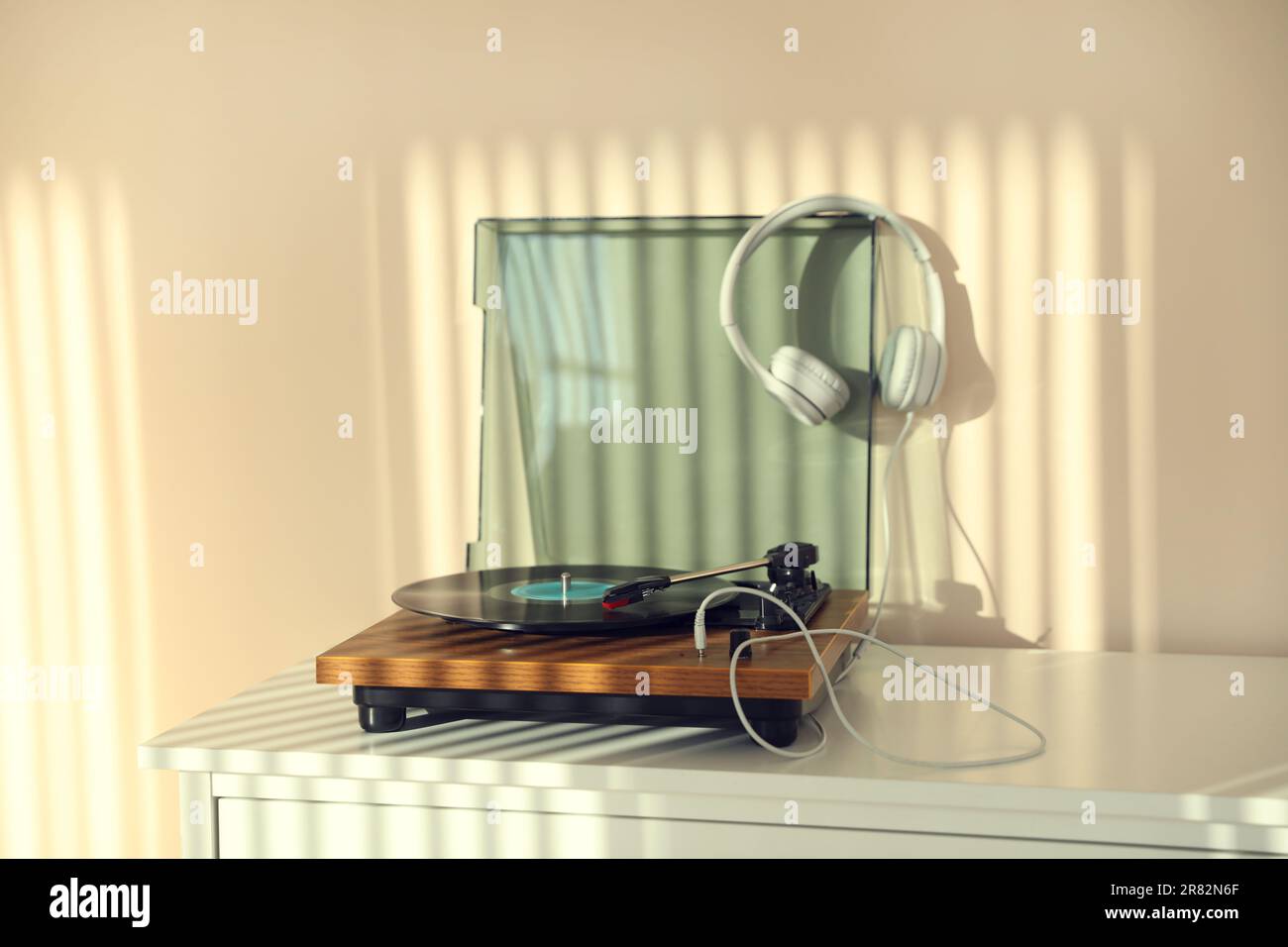 Elegante giradischi con disco in vinile e cuffie su cassettiera bianca a casa Foto Stock
