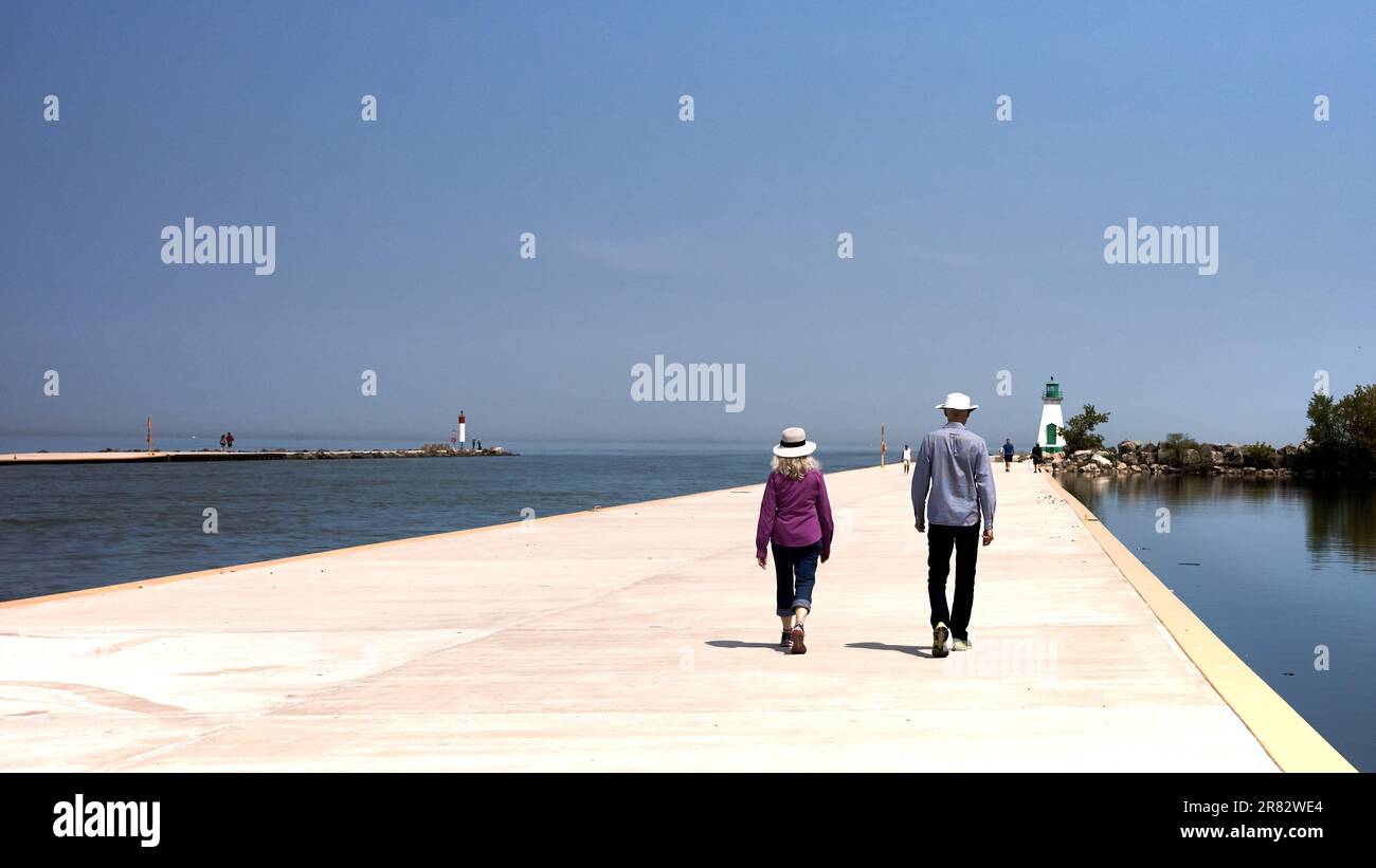 Coppia anziana alla moda camminare un lungo molo verso un faro a Port Dalhousie, Ontario, Canada. Foto Stock