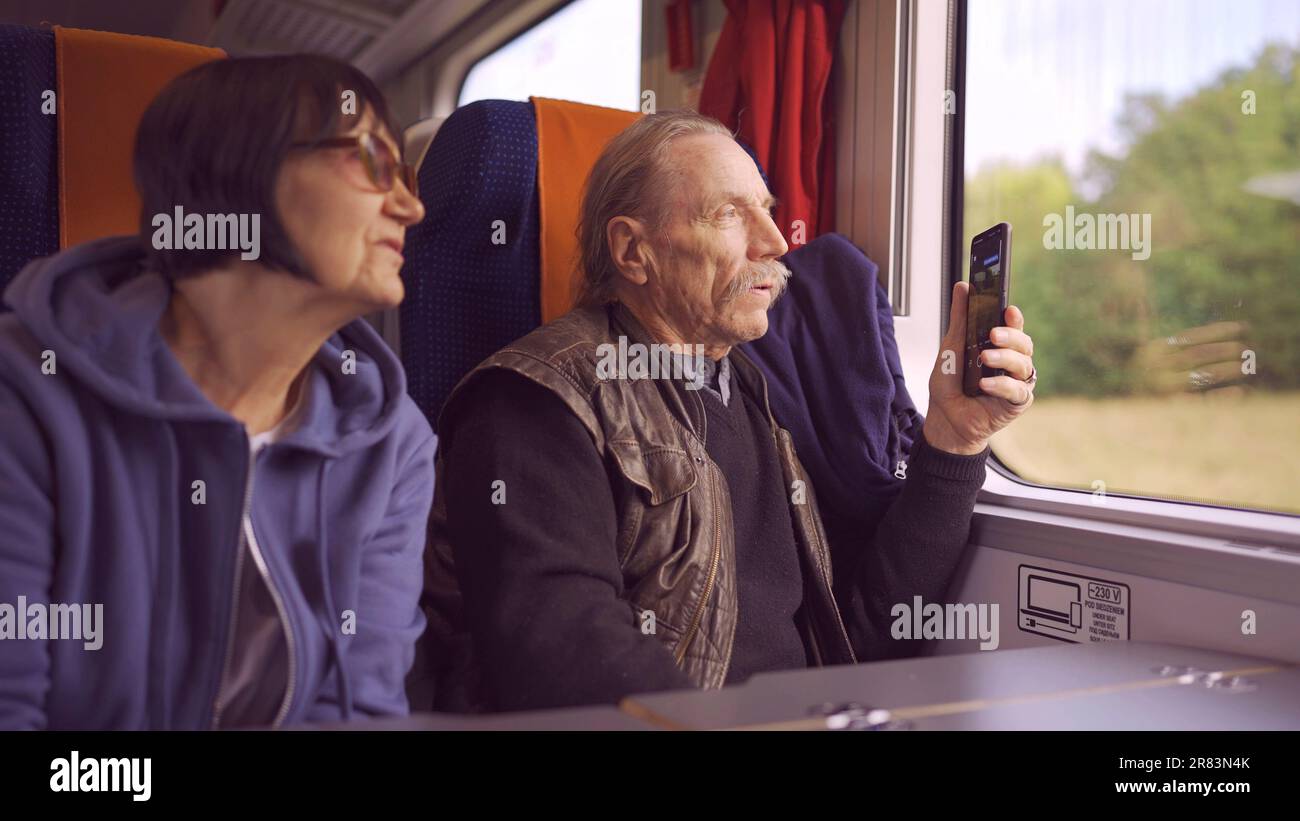 Coppie anziane viaggiano in treno, anziani guarda fuori dalla finestra e spara su un telefono cellulare Foto Stock