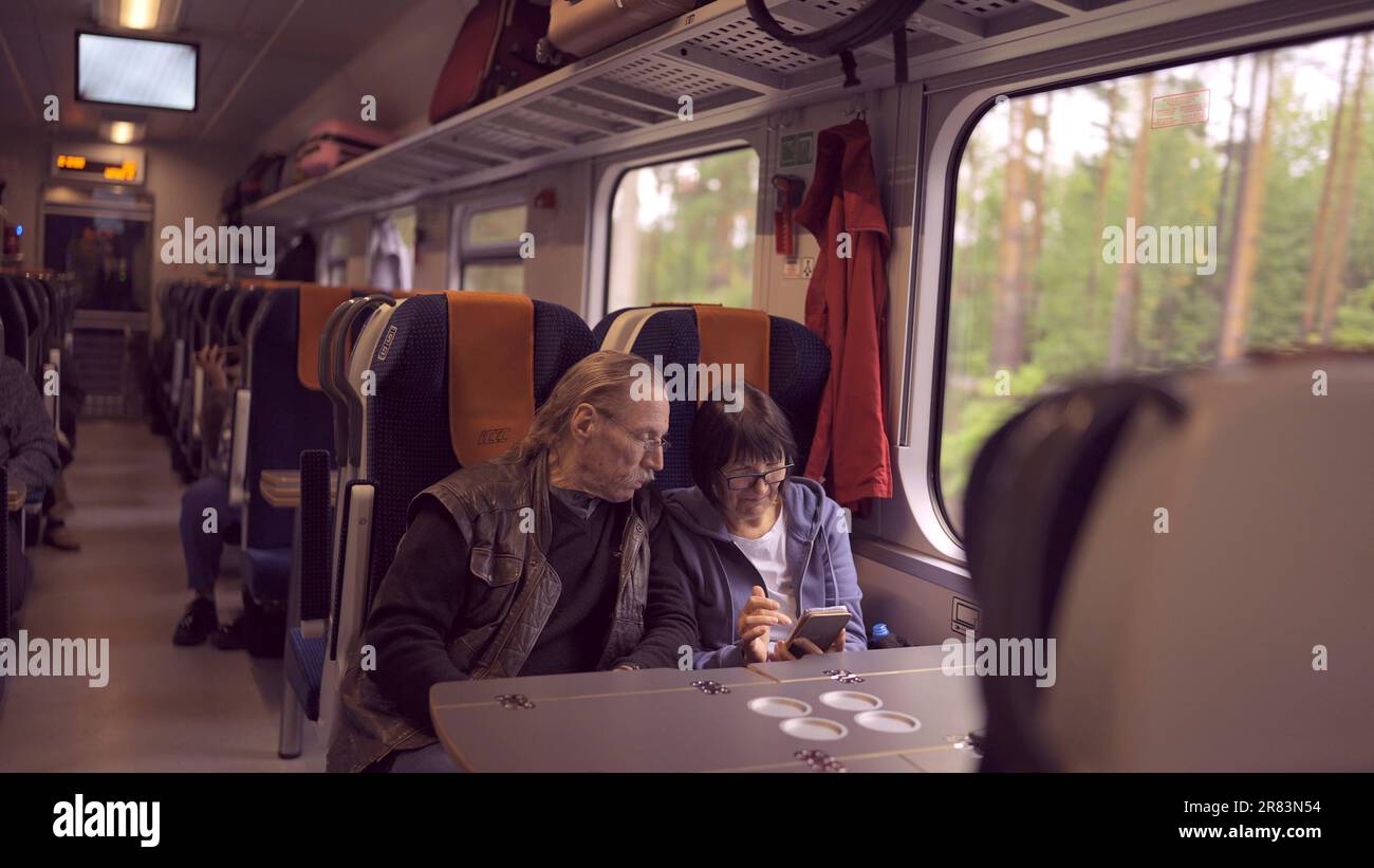 La coppia anziana viaggia in treno, la signora tiene in mano un telefono cellulare, entrambi guardano lo smartphone e parlano tra loro Foto Stock