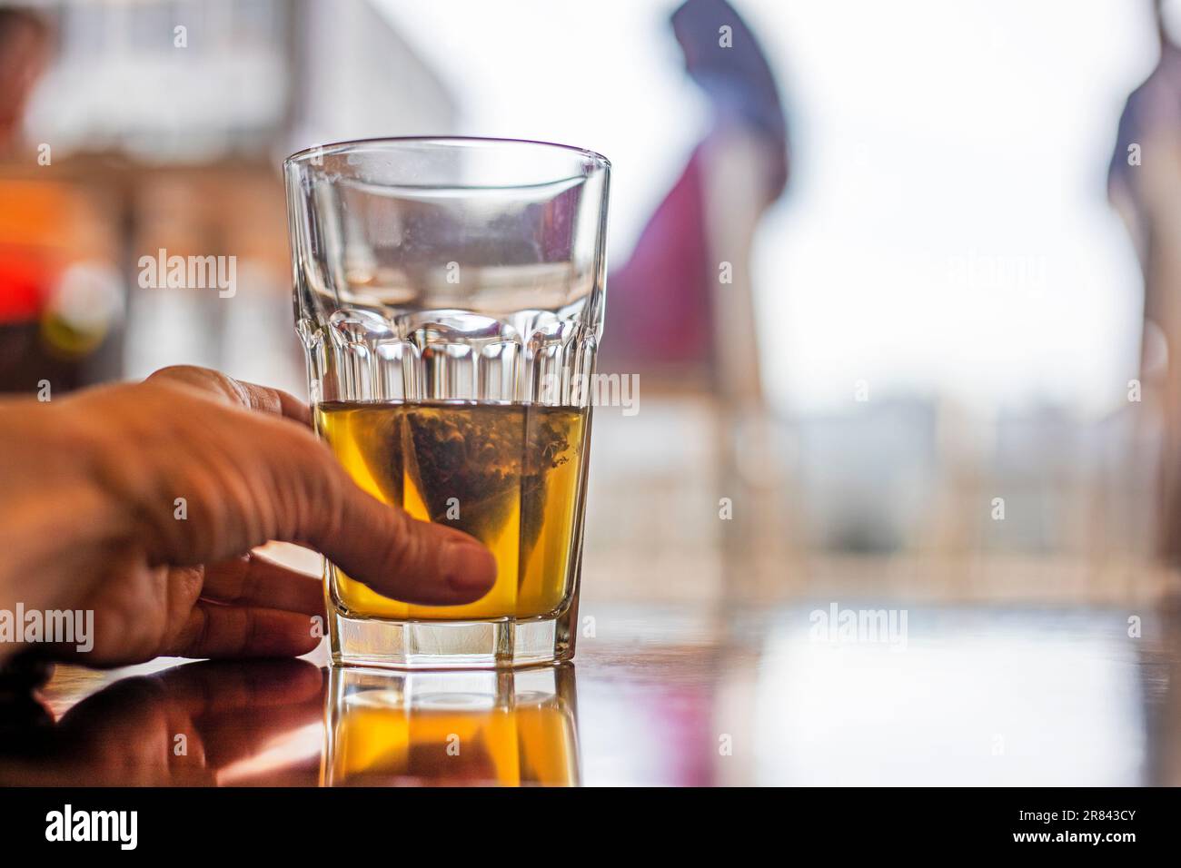 la mano della donna tiene una tazza di vetro con il tè verde in una borsa in un caffè. Snack Foto Stock