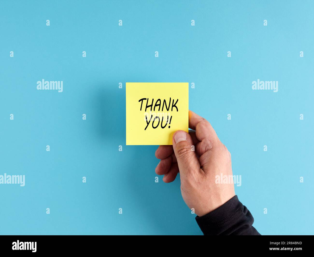 La mano maschile tiene una carta adesiva gialla con la parola grazie. Messaggio di gratitudine. Foto Stock