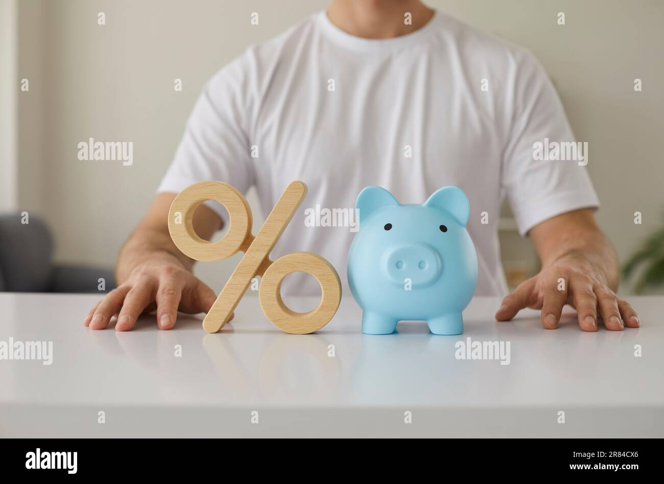 Colpo corto di un uomo seduto a un tavolo con un simbolo di percentuale e una banca piggy Foto Stock