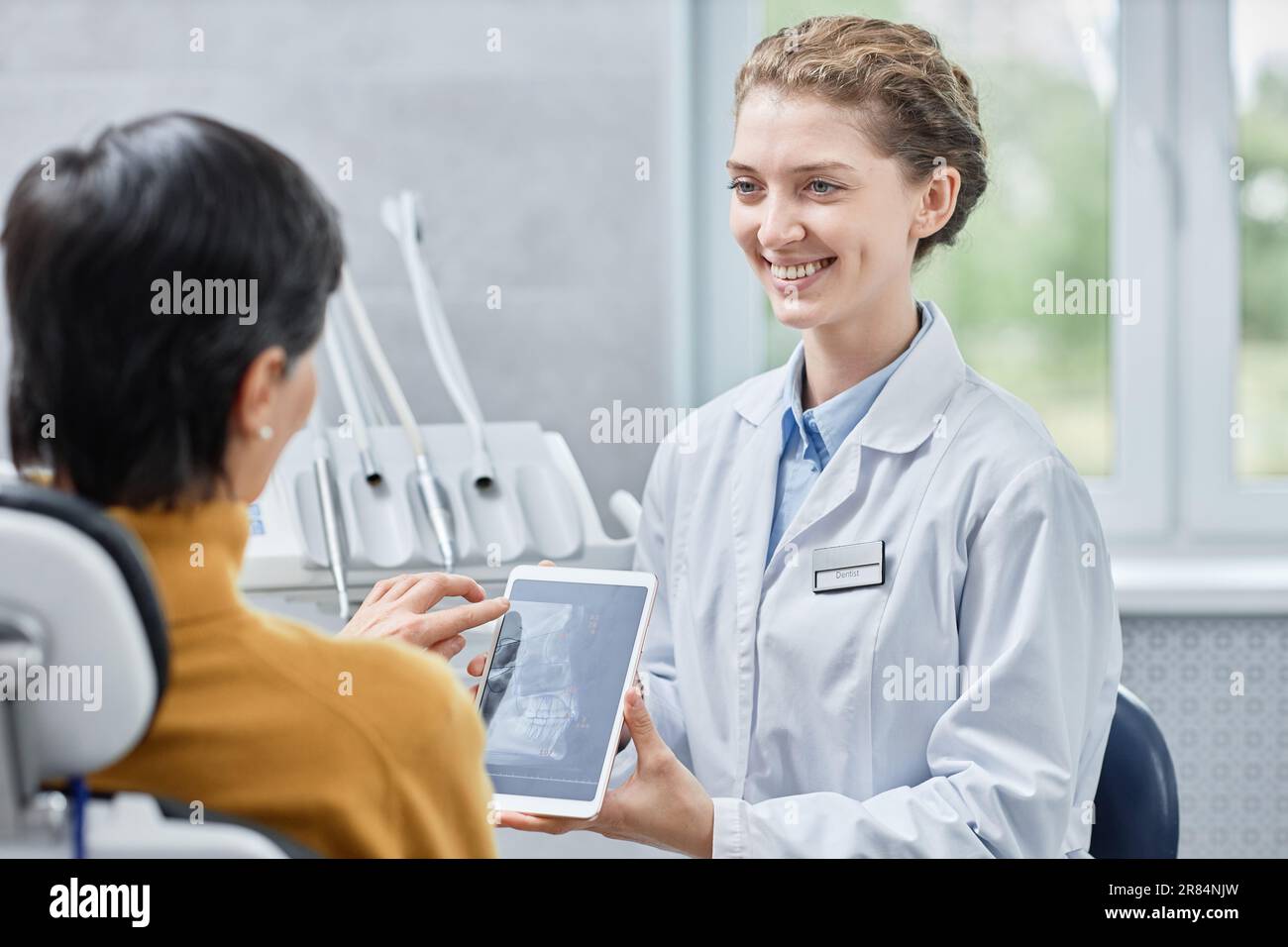 Ritratto di un dentista sorridente che mostra immagini radiografiche su tablet alla paziente in clinica Foto Stock
