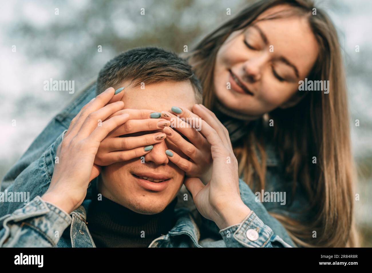 Chi è. Una donna felice chiude gli occhi di un uomo con un sorriso attraente con le sue mani Foto Stock