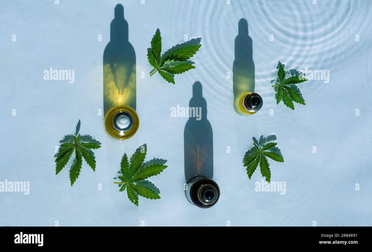 Bottiglie di olio CBD, sfondo blu con gocce, onde e foglie di canapa, marijuana Foto Stock